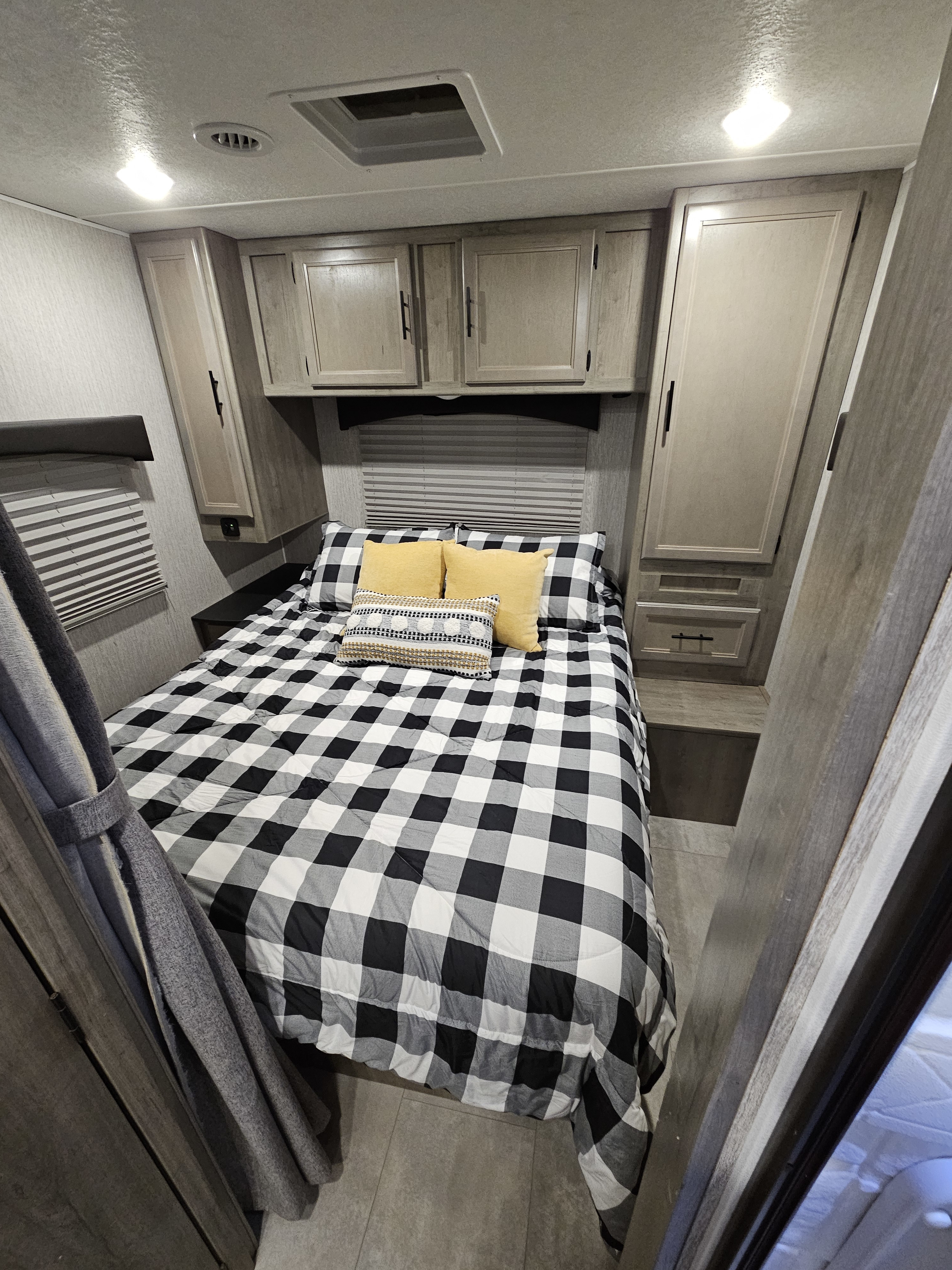 Cozy RV rental bedroom featuring a black and white buffalo check bed, bright lighting, and overhead cabinets.. Coachmen Freelander 27QB 2022