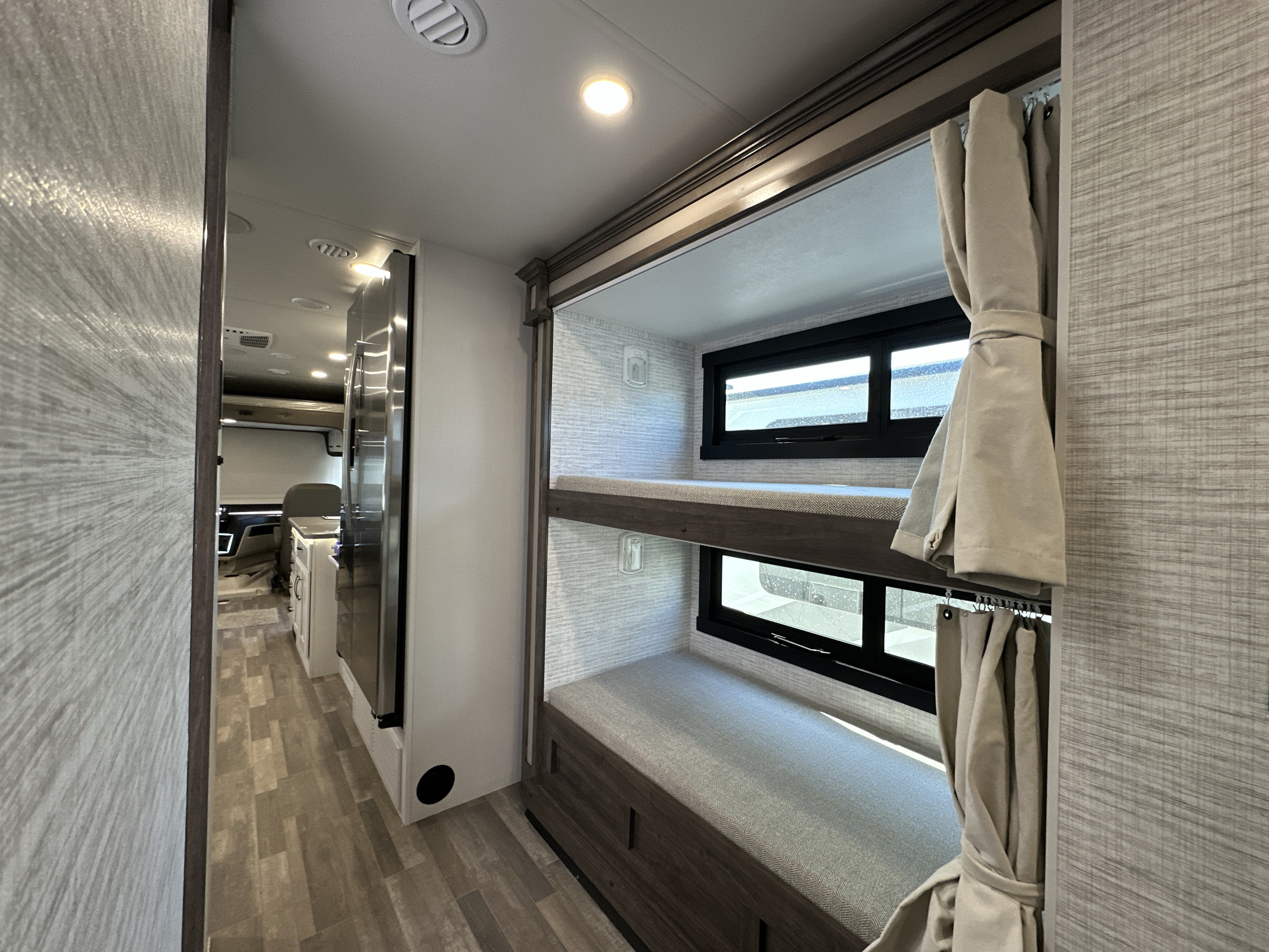 This RV rental offers comfortable, modern bunk beds with windows and tied-back curtains. A hallway leads to the kitchen area.. Entegra Coach Vision XL 36A 2025