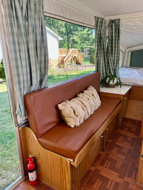 Discover a cozy RV rental interior: brown bench, plaid curtains, wood-look floor, and a scenic outdoor view. Fire extinguisher visible.. Starcraft Starcraft Popup Trailer 2003