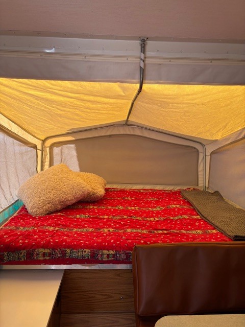 Enjoy a cozy night in this pop-up camper bed, featuring a red quilt and fluffy pillows. Ideal for your next RV rental experience.. Starcraft Starcraft Popup Trailer 2003