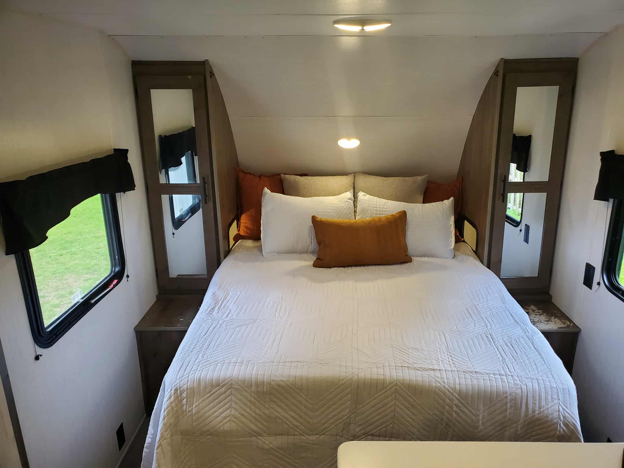 This RV rental's cozy bedroom features a spacious bed, mirrored closets, and windows with scenic views.. Heartland RVs Pioneer 2023