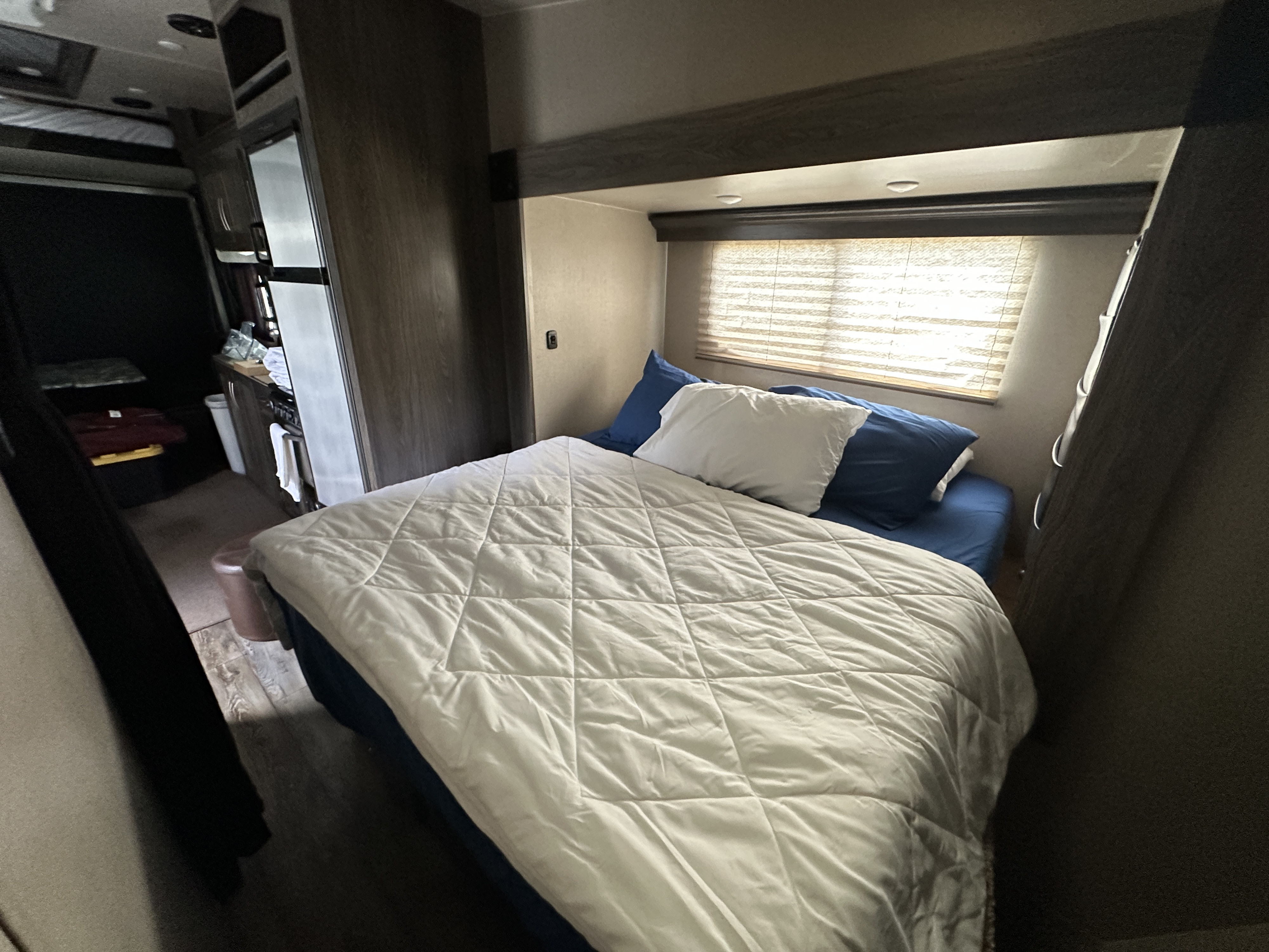 Inside an RV rental, a comfy bedroom features a white comforter, blue pillows, and window blinds. Compact living space.. Genesis Supreme Rv Vortex 2019