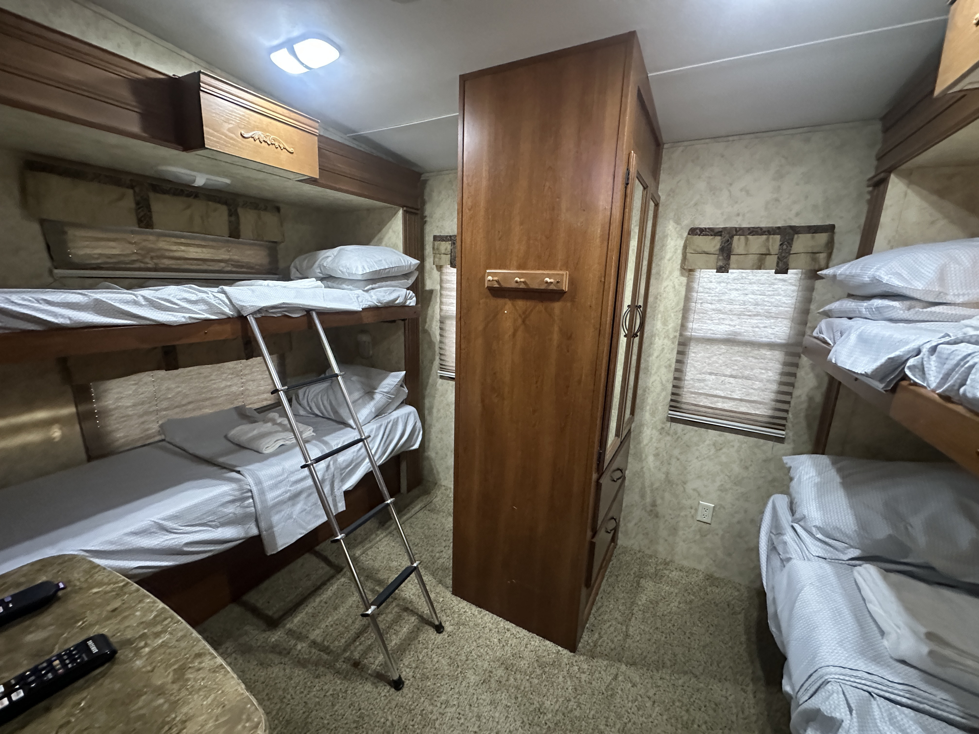 RV rental bunkhouse: A compact sleeping area with two bunk beds, light sheets, a ladder, and central wardrobe.. Keystone RV Montana High Country 2010