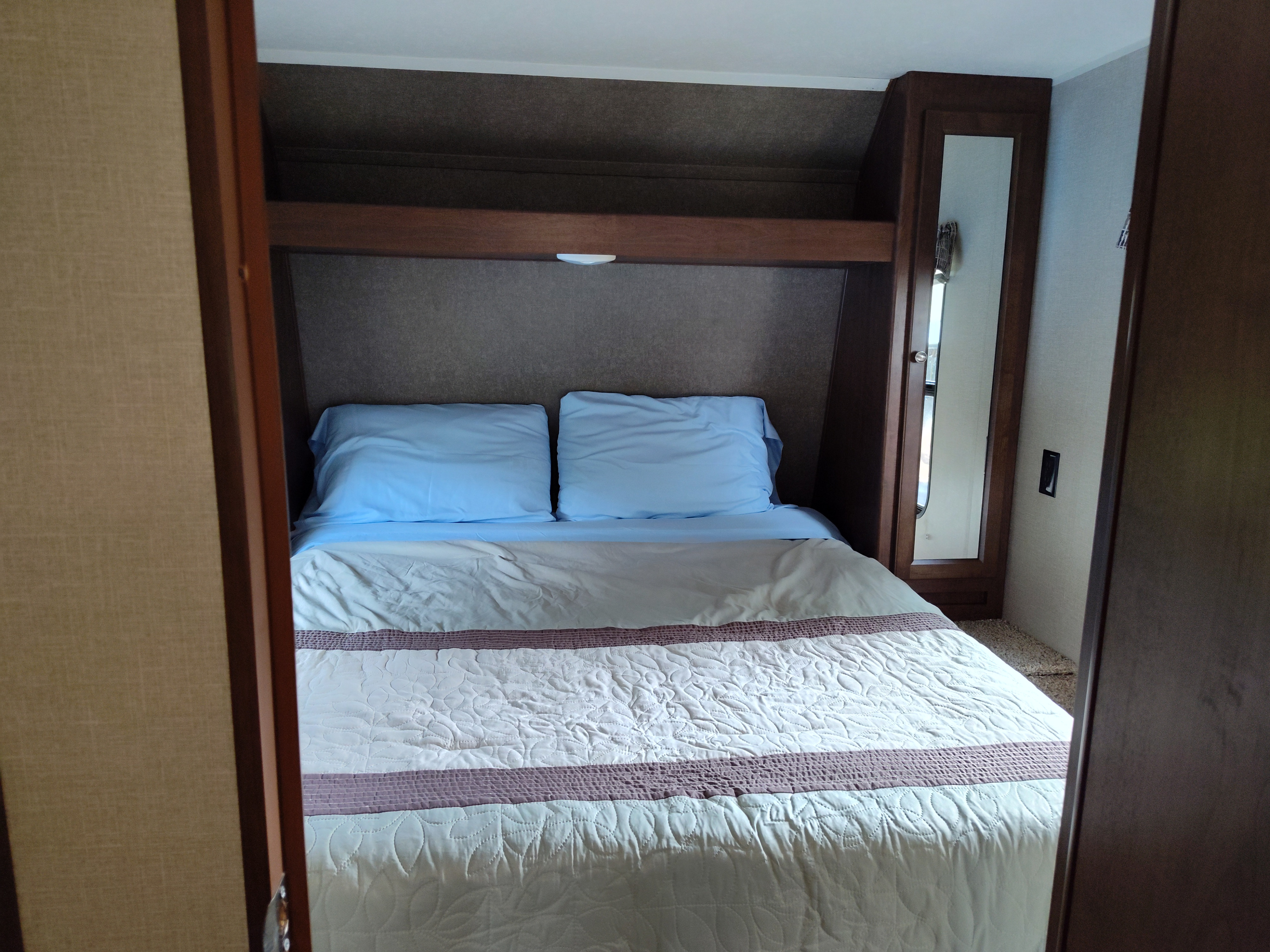 A compact RV rental bedroom. Features a comfortable bed with blue pillows, quilted blanket, and convenient overhead storage.. Keystone Hideout 28BHS 2017