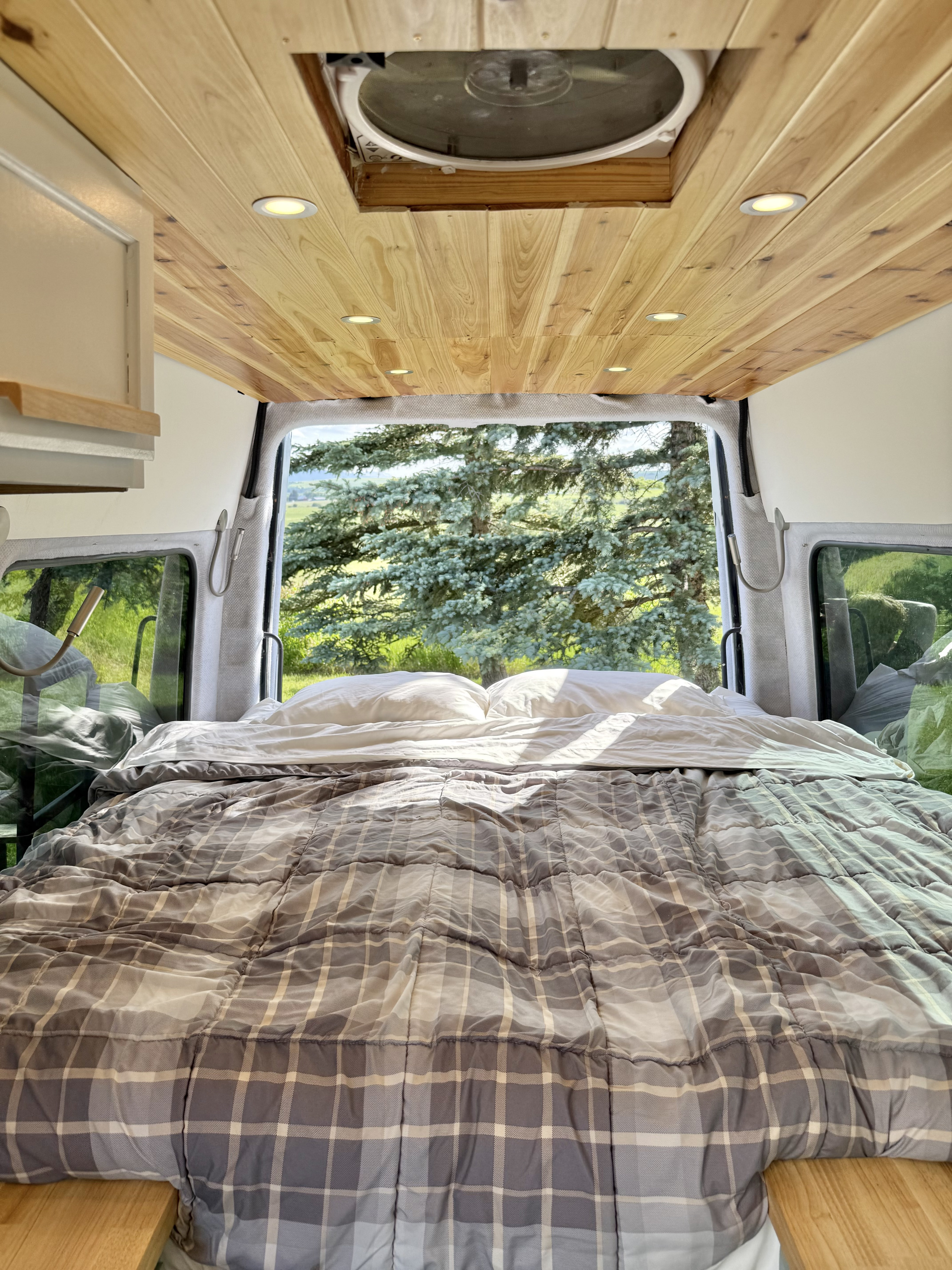 Cozy RV rental bedroom in a camper van, featuring a plaid bed, wooden ceiling, and an expansive nature view from the open back.. Dodge Sprinter 2500 170ext 2008