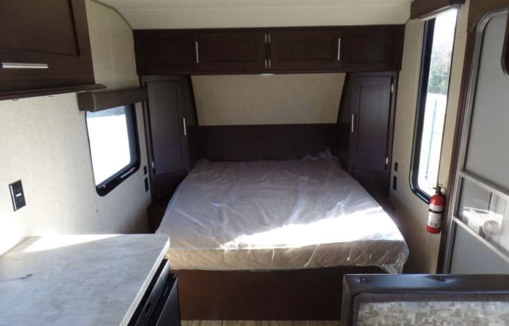 Clean RV rental bedroom showing a bed with plastic cover, dark cabinets, bright windows, and fire extinguisher.. Forest River Wolf Pup 2017