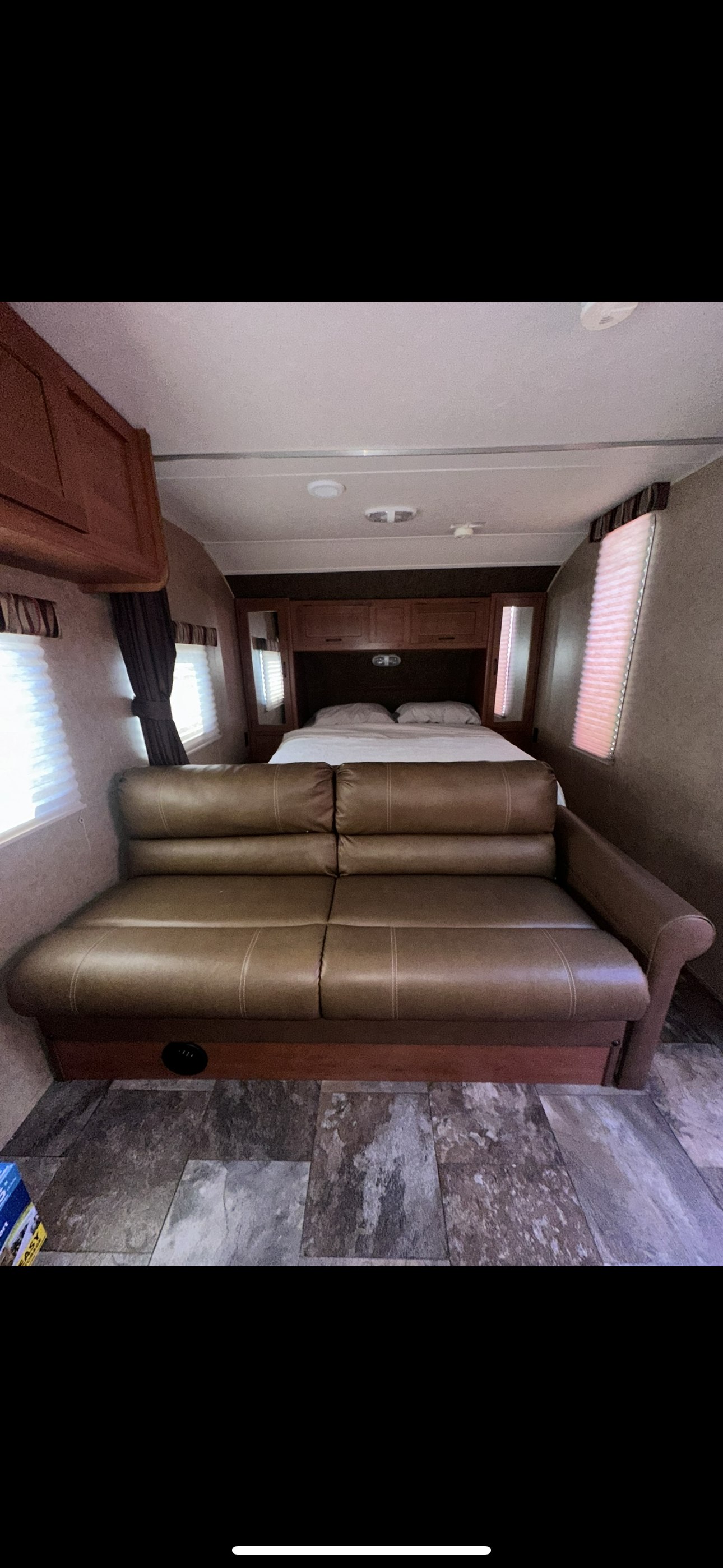 RV rental interior featuring a brown couch, bed in the rear, and bright windows, offering a cozy living space.. Forest River Cherokee Grey Wolf 2014
