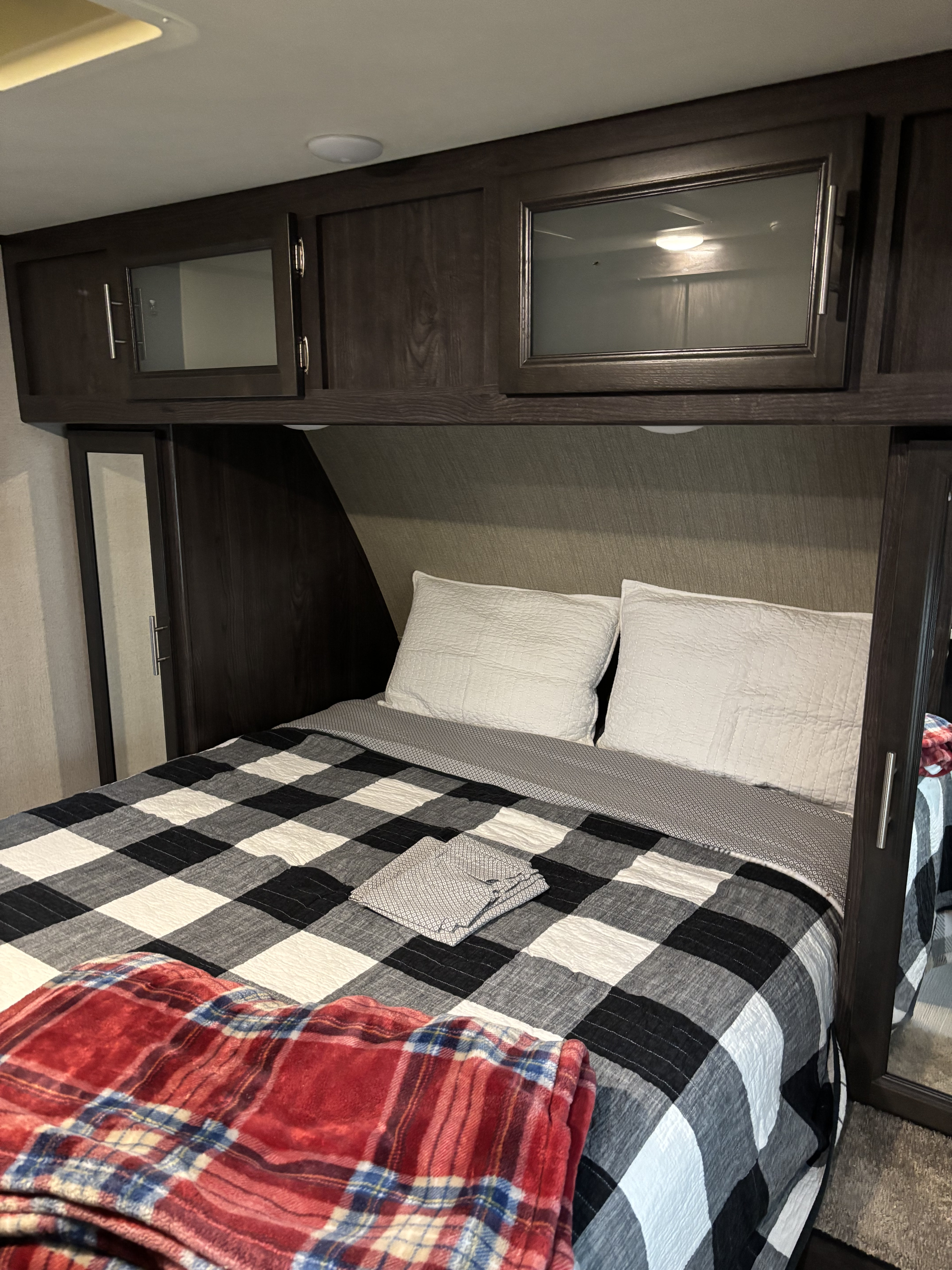 Cozy RV rental bedroom featuring a bed with a black and white plaid quilt, white pillows, and dark wood cabinets.. Dutchmen Kodiak Express 2018