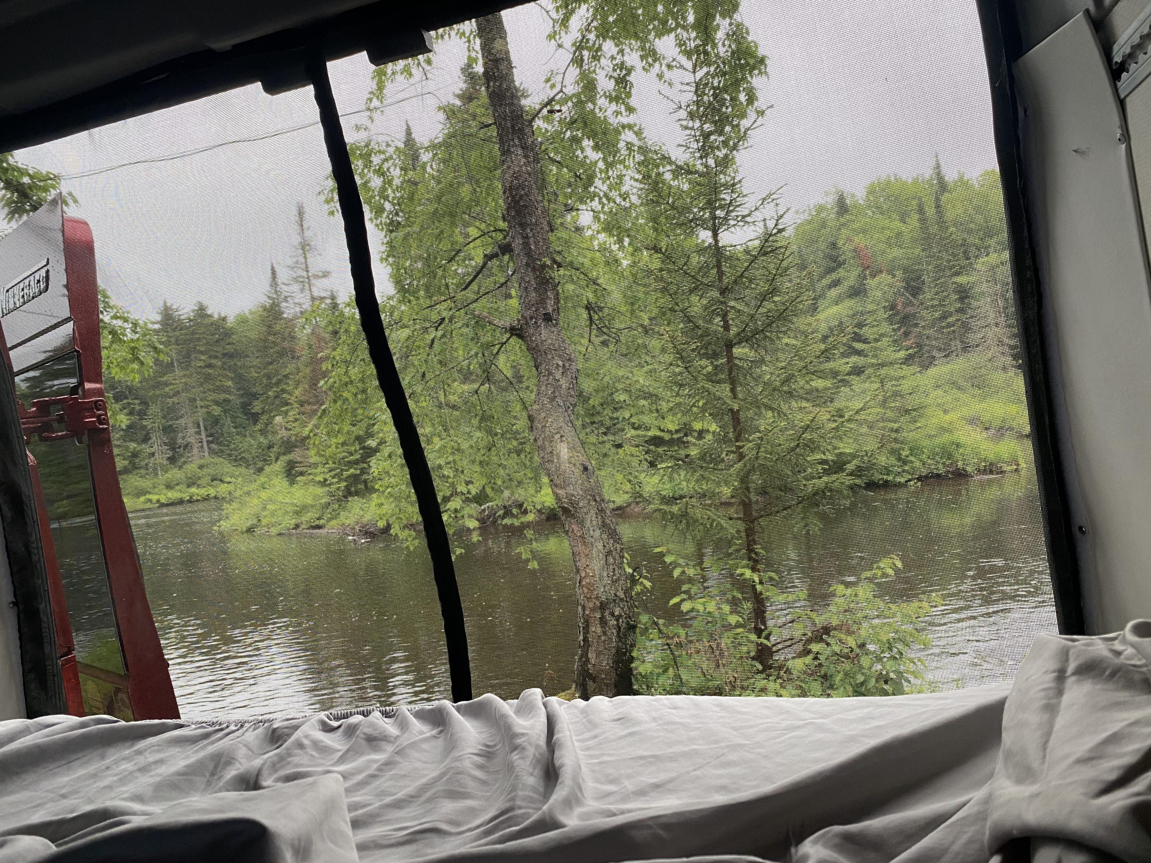 Enjoy a serene RV rental view from bed, featuring a screen window overlooking a tranquil lake and lush forest.. Winnebago Solis PX 2021