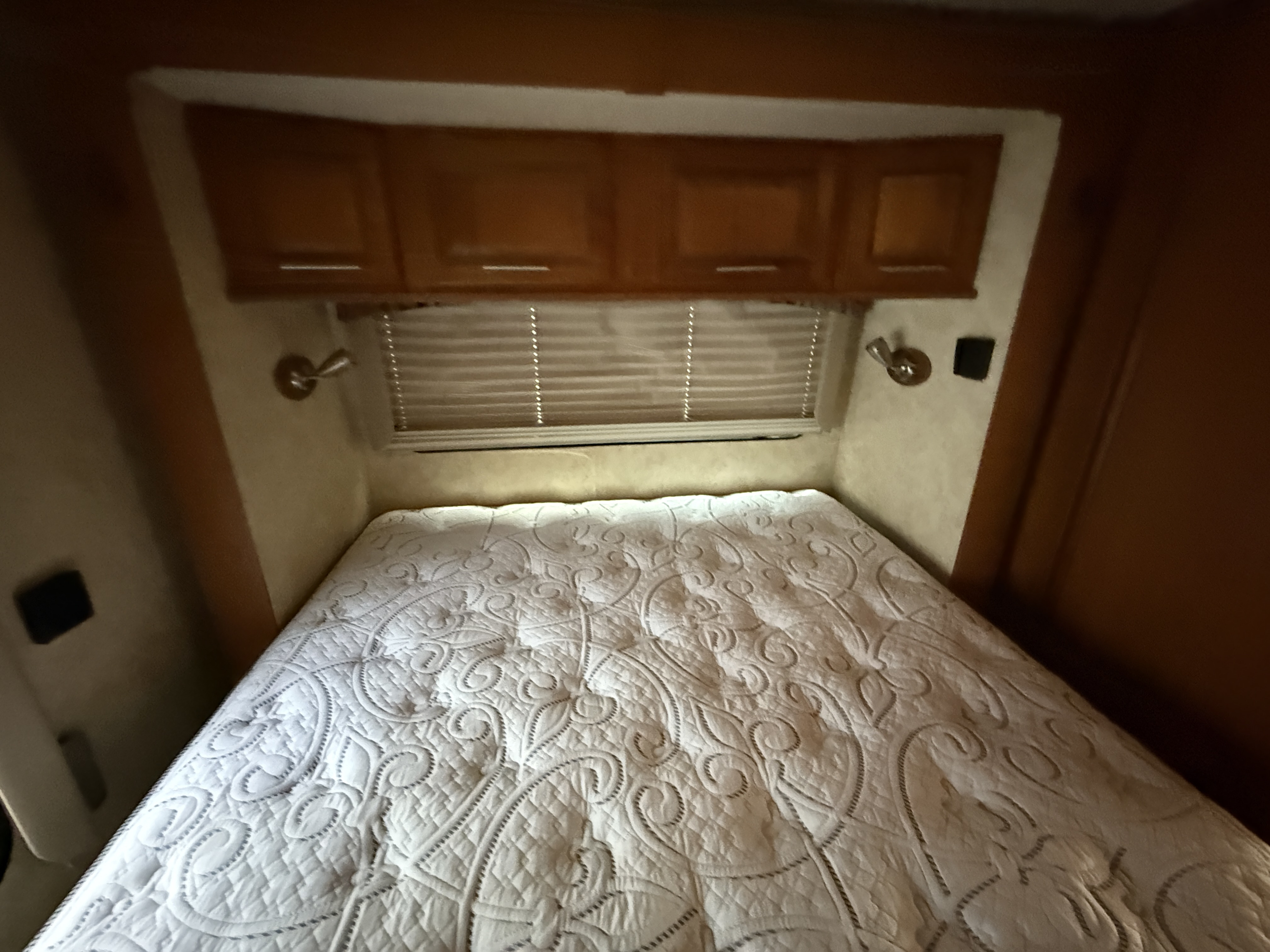 RV rental bedroom: a comfortable bed with quilted mattress, overhead wood cabinets, and window blinds.. Forest River Coachmen Concord 2012