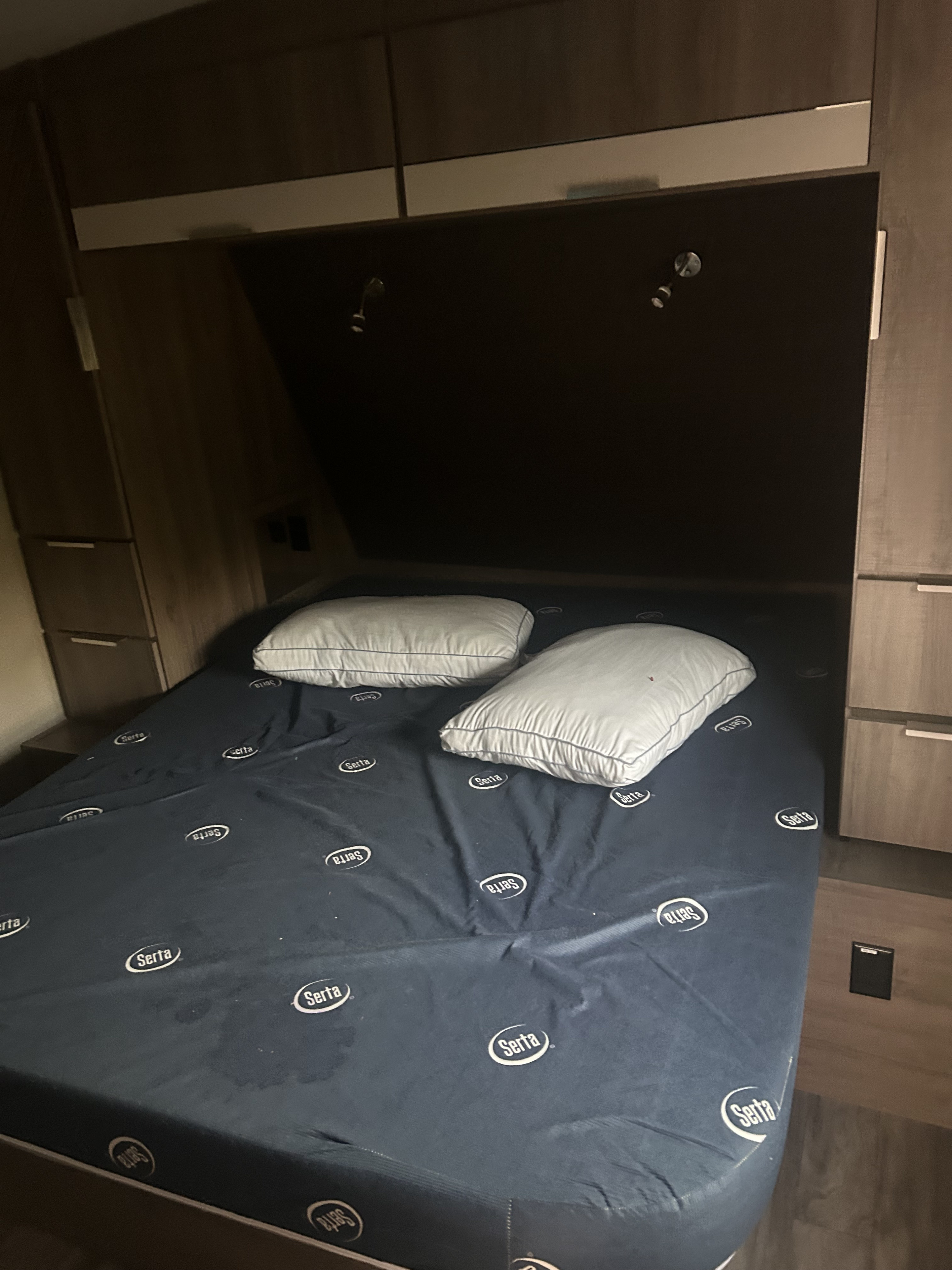 Cozy RV rental bedroom features a bed with a Serta mattress cover, pillows, and integrated storage cabinets.. Grand Design Imagine 2021