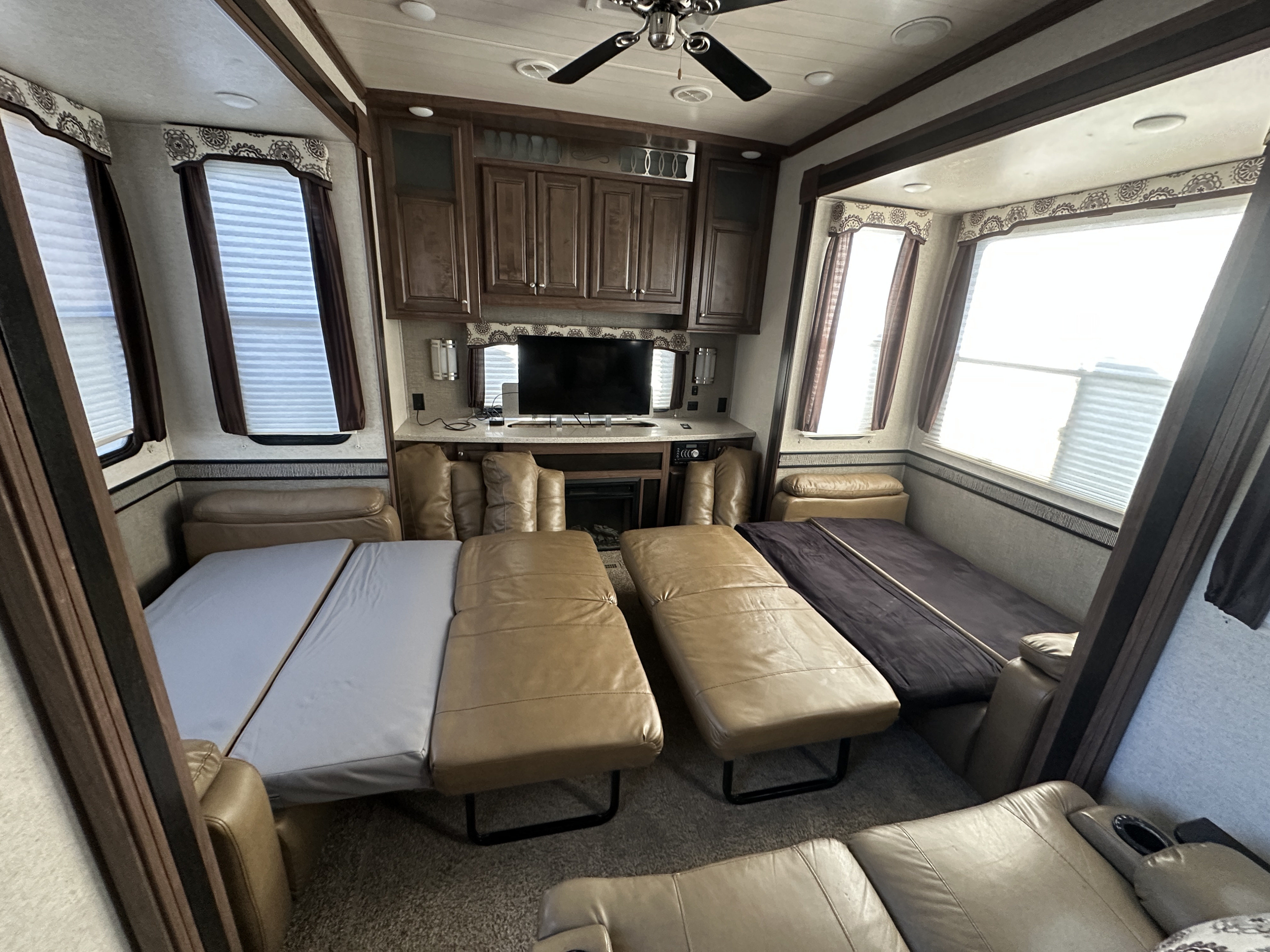 This RV rental interior features a living area with convertible recliners/beds, TV, fireplace, and multiple windows.. Heartland RVs Oakmont 2016