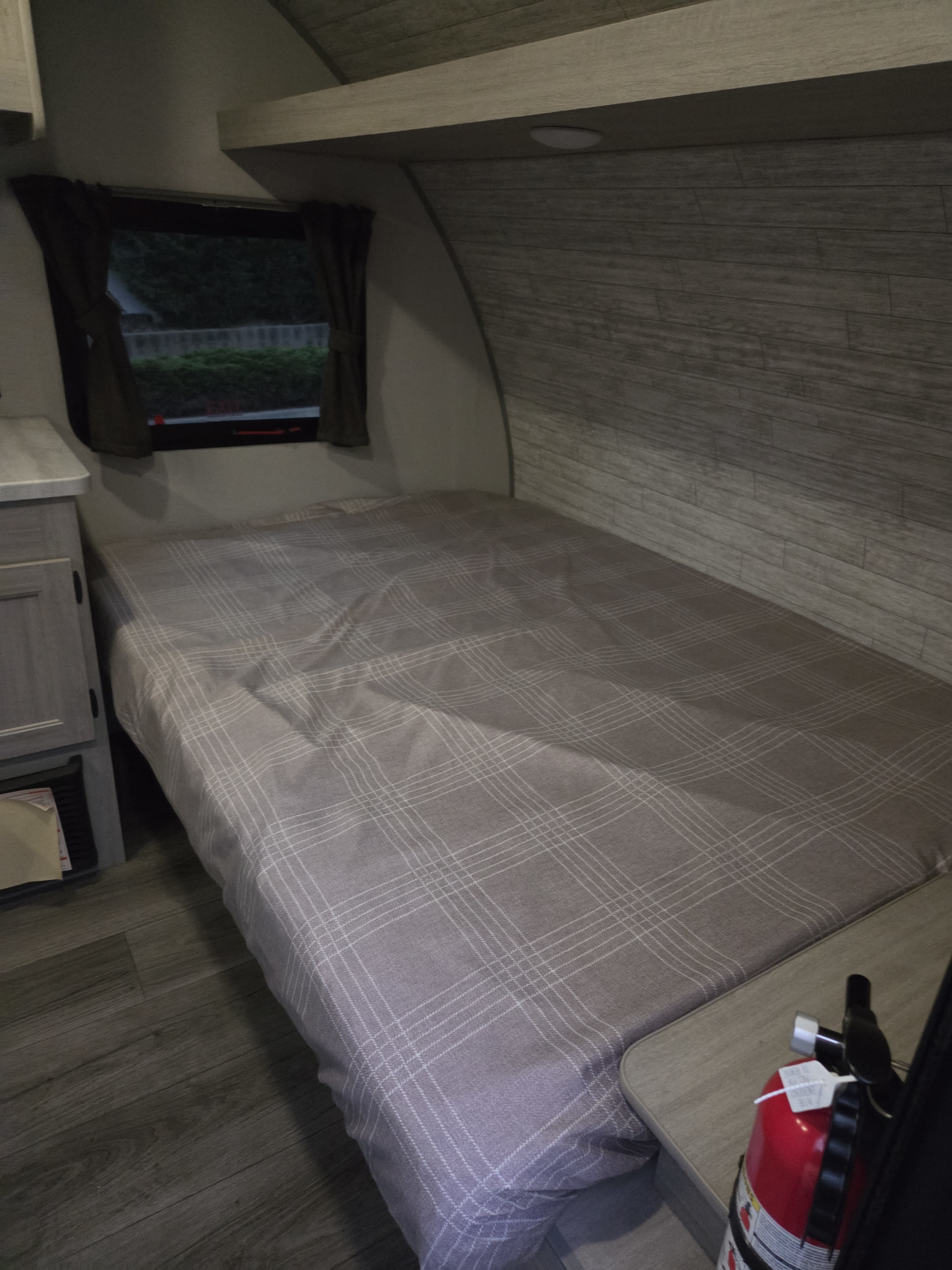 Cozy RV rental bedroom featuring a plaid bed, window with curtains, and a visible fire extinguisher for safety.. Coachmen Catalina Summit 134BHX 2025