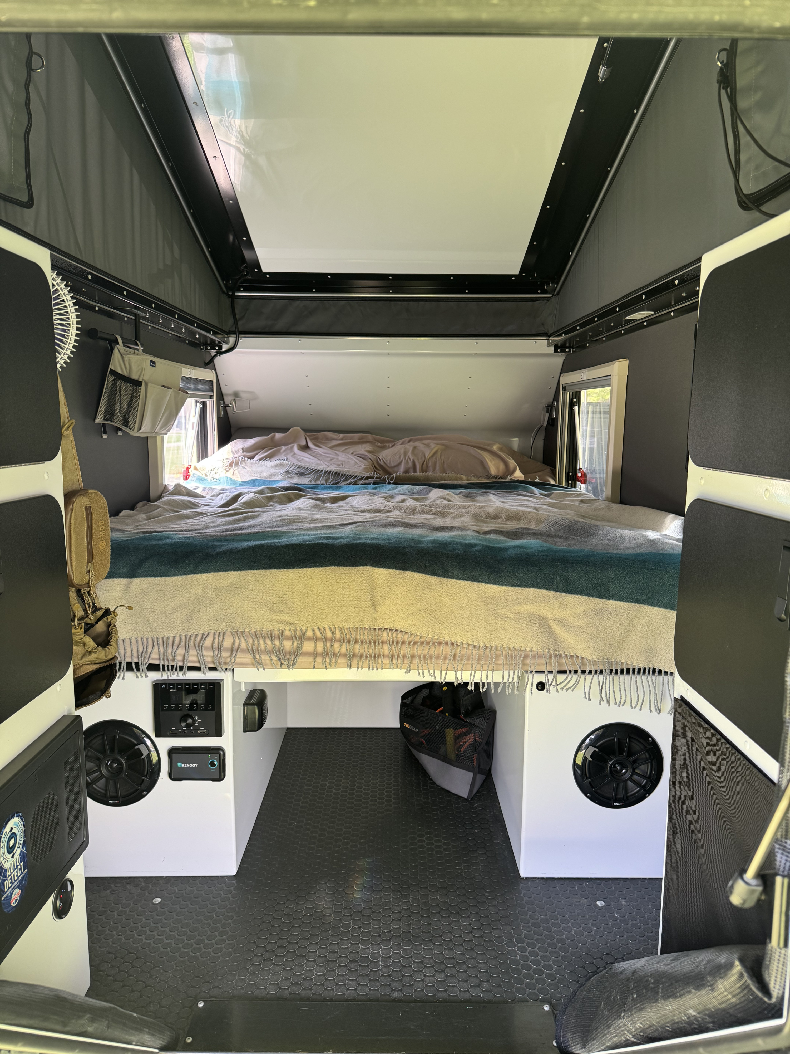 Explore this RV rental's cozy interior: a comfortable bed, control panel, speakers, and practical under-bed storage.. Mission Overland Summit 2024