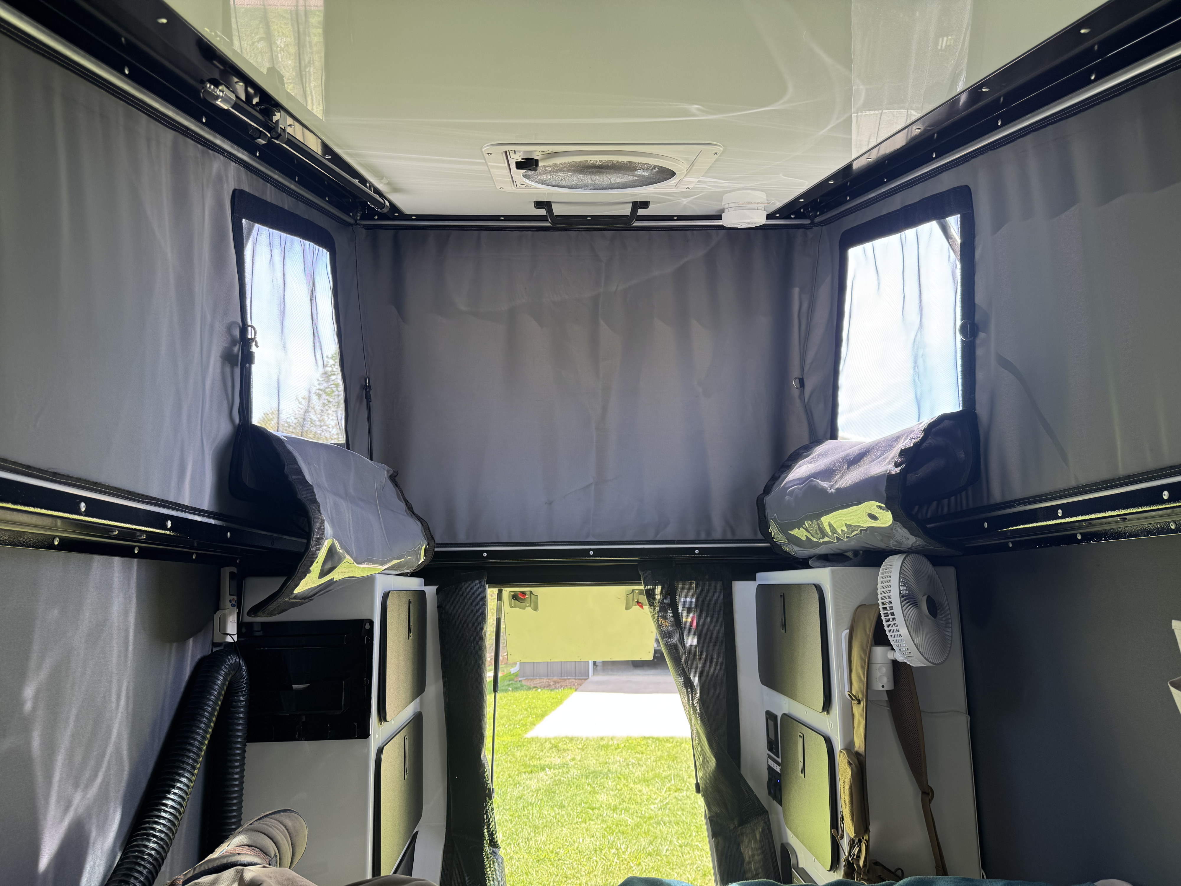 Interior of an rv rental pop-top camper, with ceiling fan, mesh windows, storage, and outdoor view.. Mission Overland Summit 2024
