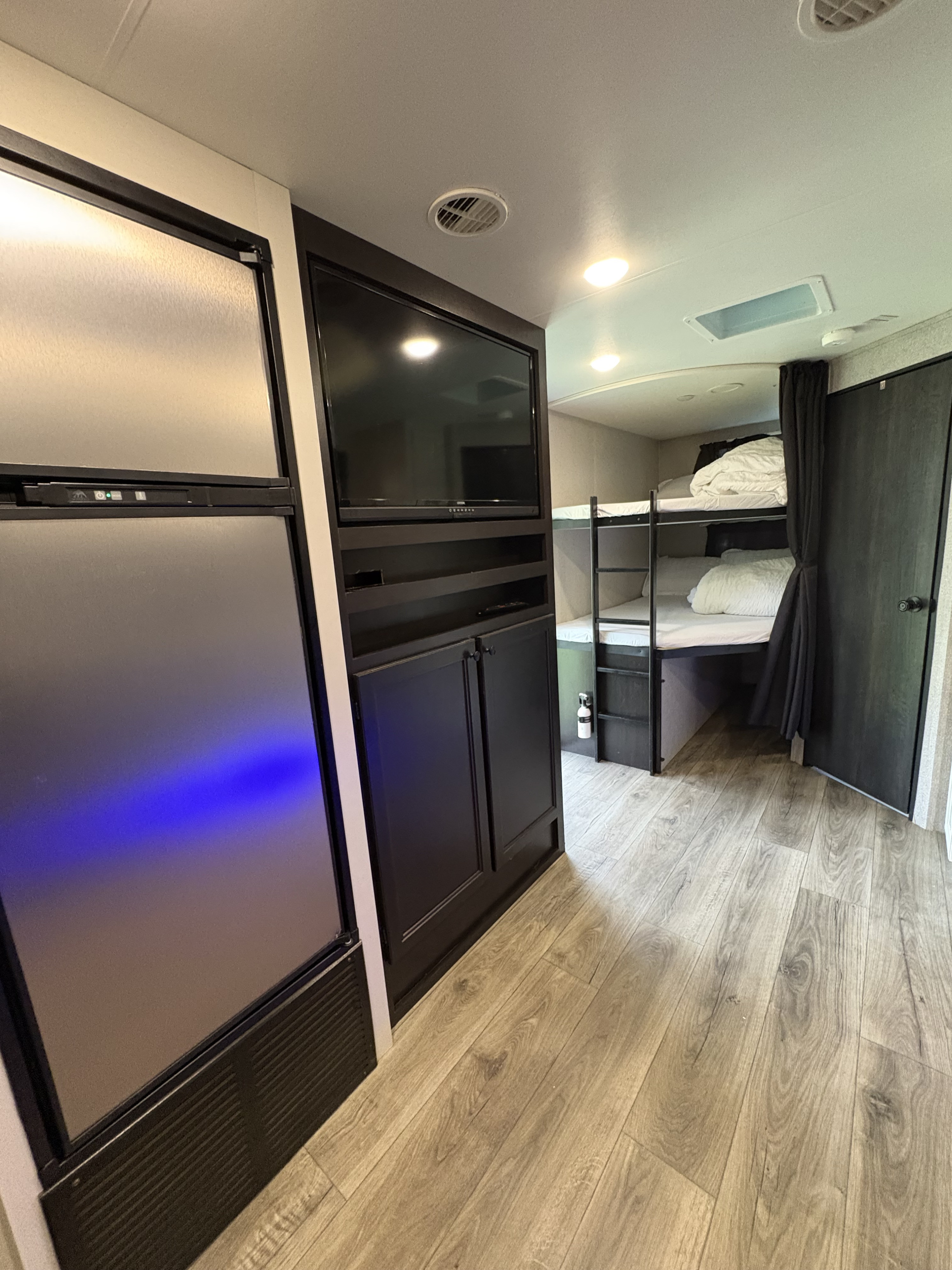 This RV rental interior features bunk beds with a privacy curtain, a TV, refrigerator, and wood-look flooring.. Highland Ridge RV Range Lite 2021