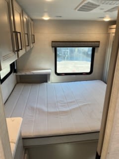 This modern RV rental bedroom features a clean white mattress, overhead cabinets, and a window, ideal for your next trip.. Thor Motor Coach Chateau 2024