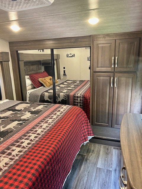 Rustic RV rental bedroom: cozy buffalo plaid & deer bedding, mirrored closet, wood-toned cabinets, and flooring.. Keystone RV Cougar 2022