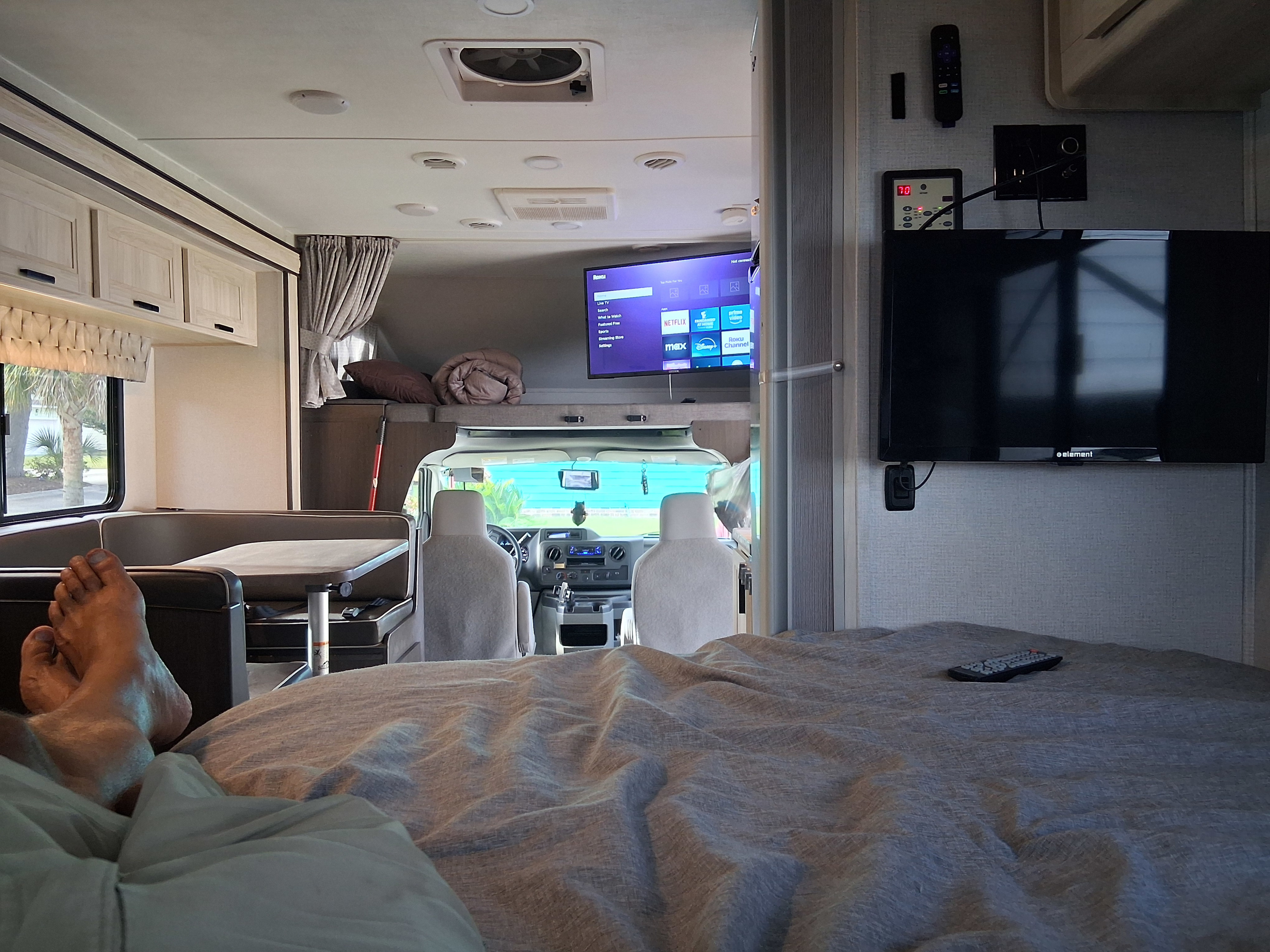 Cozy RV rental interior: feet up on bed, watching streaming TV (Roku, Netflix) while parked, with the dinette and cab visible.. Forest River SLE 2021