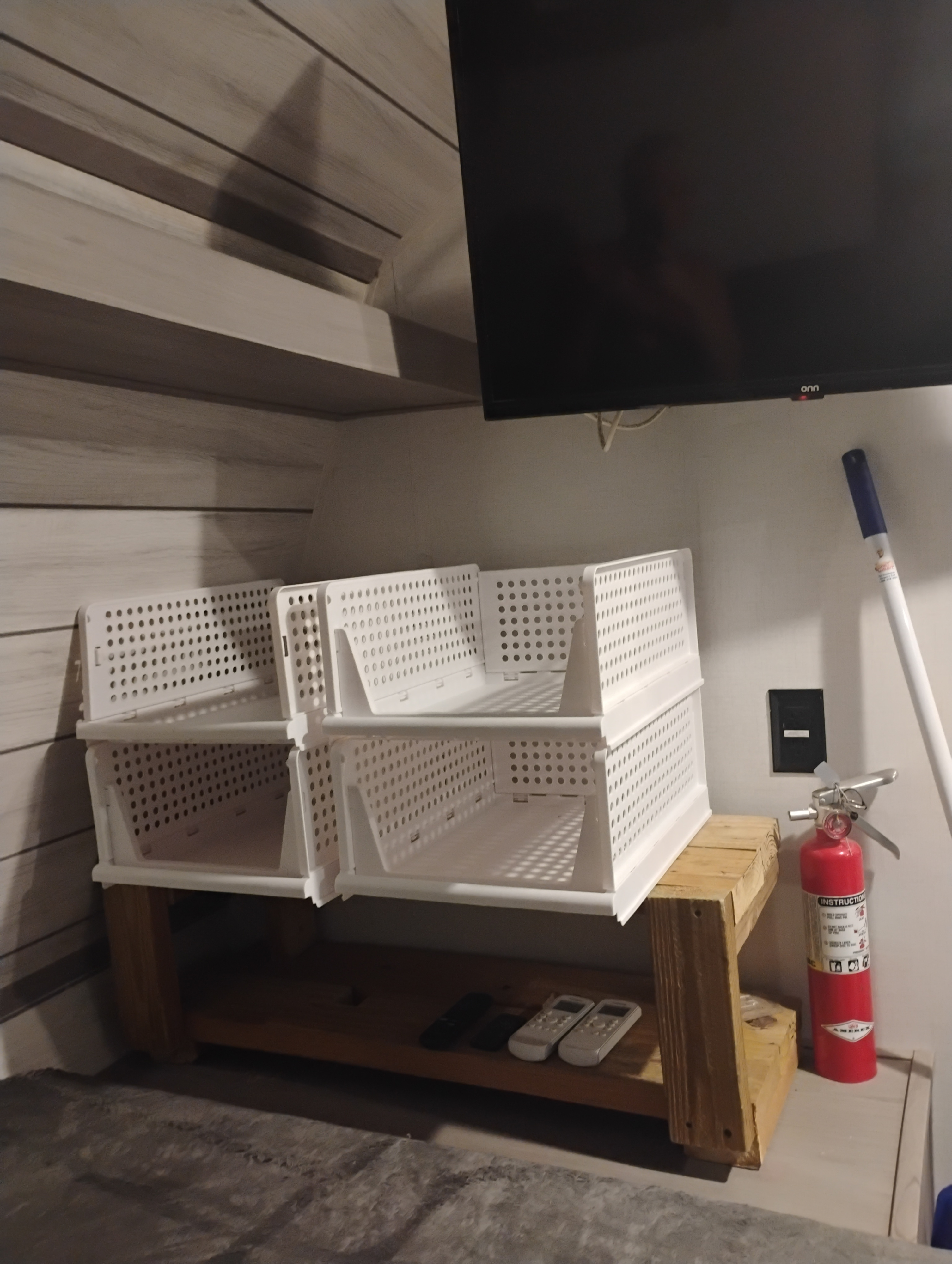 Efficient RV rental storage: White stacking bins on a wooden stand, remotes, fire extinguisher, and TV in a cozy interior.. Dutchmen Coleman Lantern 2023