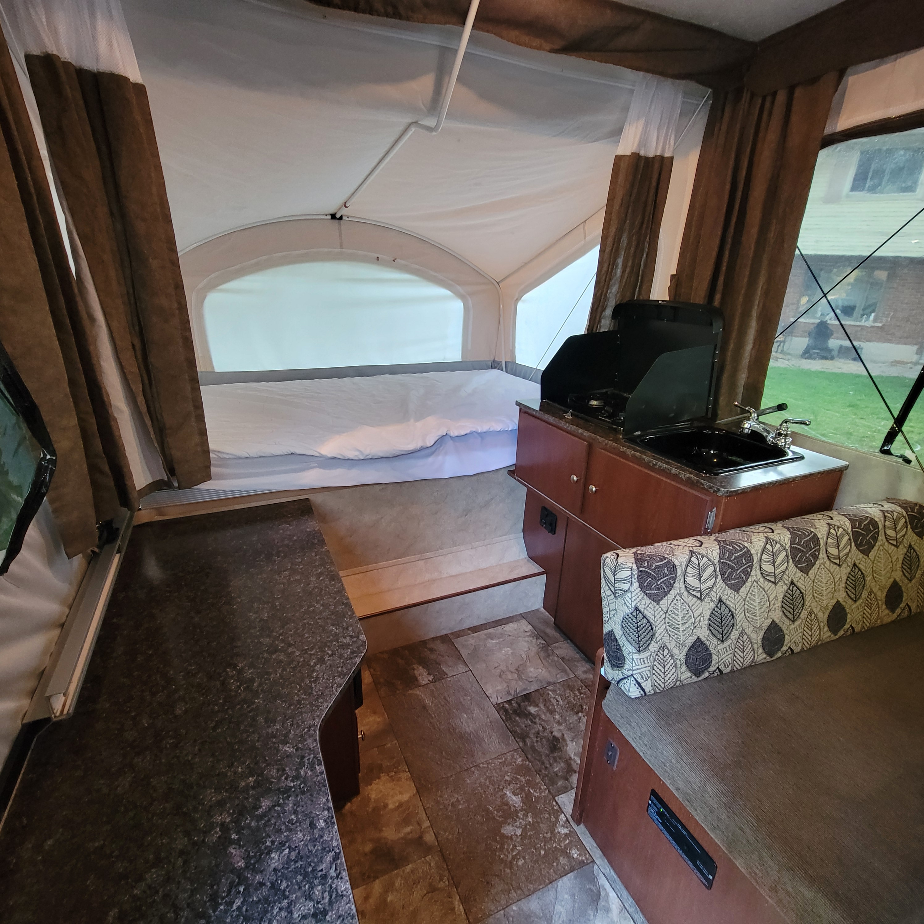 Pop-up camper RV rental interior: bed, kitchenette with sink/stove, patterned bench seating, and brown curtains.. Coachmen Clipper Sport 2015