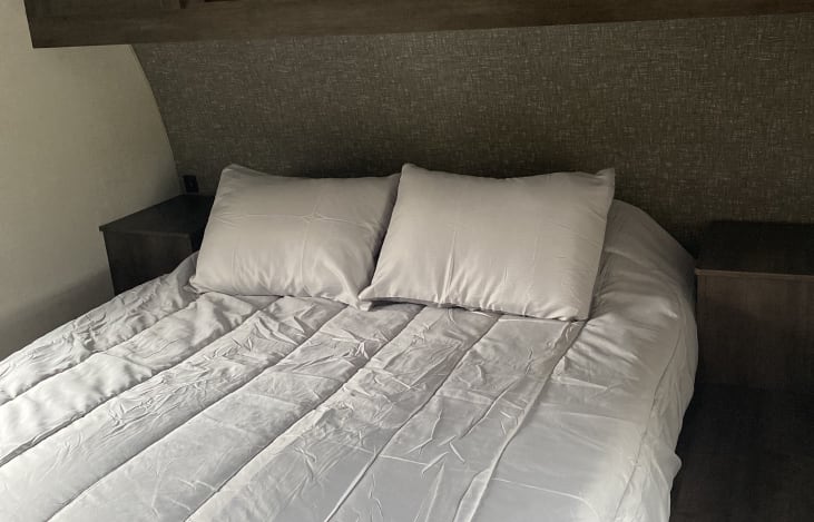 Cozy RV rental bedroom featuring a neatly made bed with white pillows, light comforter, and bedside tables.. KZ Sportsmen SE 2020
