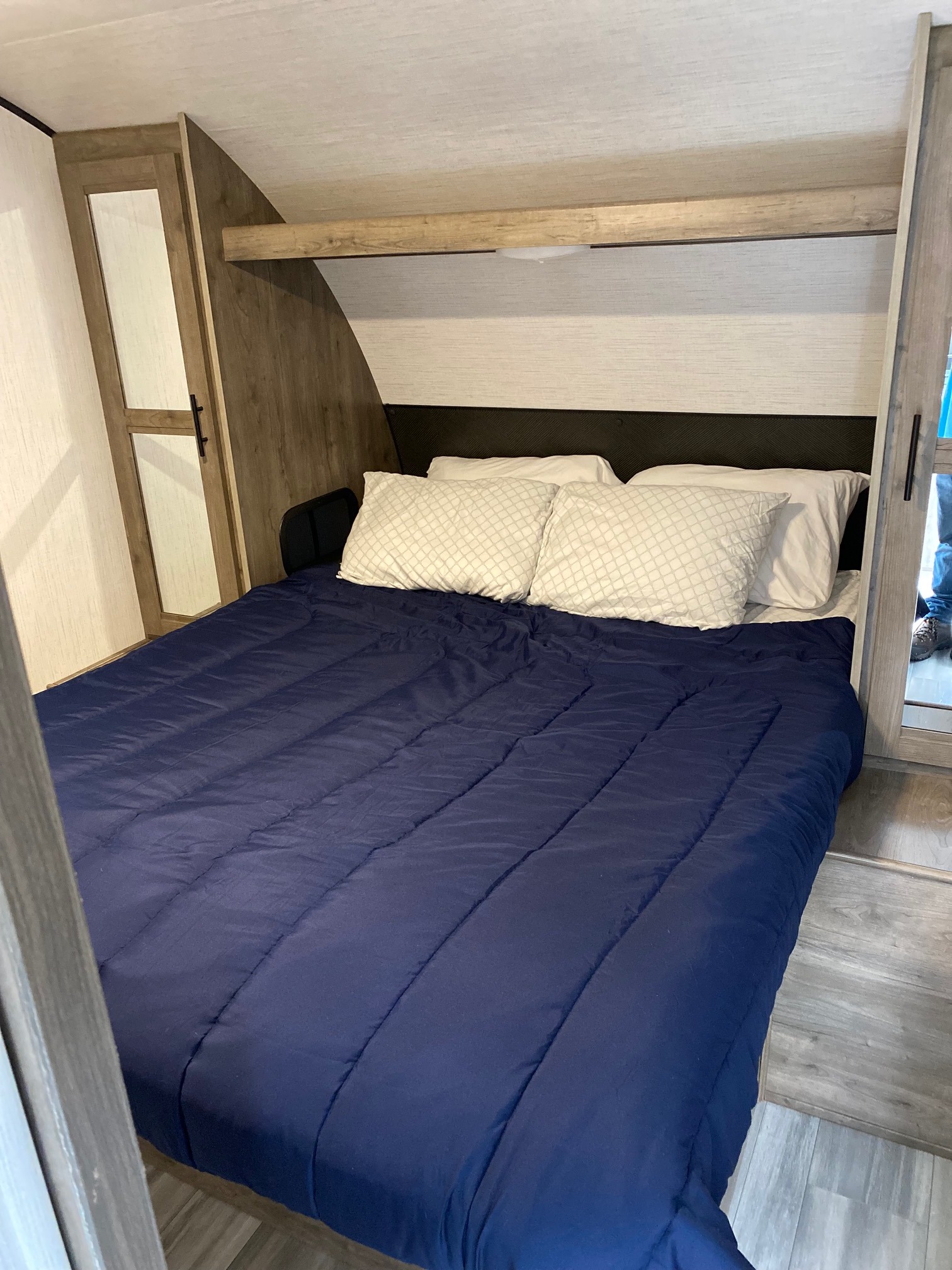 This cozy RV rental bedroom features a comfortable bed with a blue comforter and built-in mirrored closets.. Heartland RVs Pioneer 2021