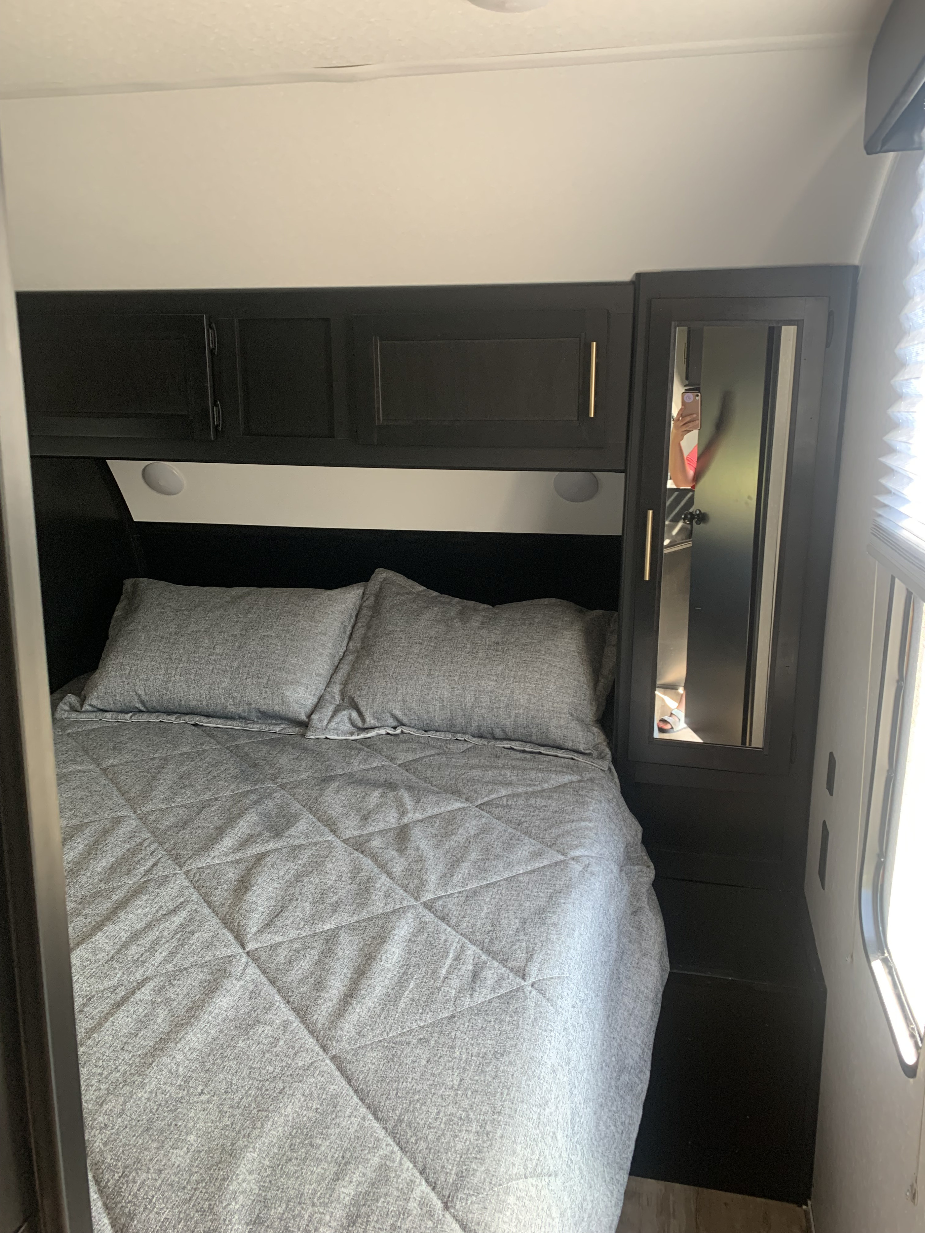 Cozy RV rental bedroom with a gray quilted bed, dark overhead cabinets, and a mirrored wardrobe.. Forest River Cherokee Patriot 2.5 2022