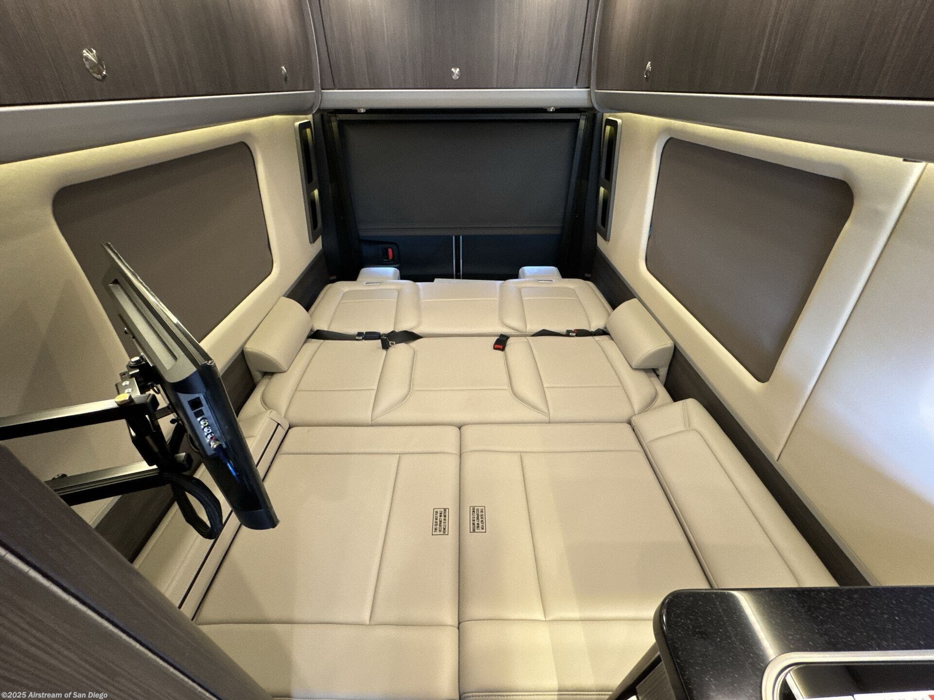 RV rental: Cream convertible bed/seating area in a modern camper van interior, complete with overhead storage and TV.. Airstream Mercedes-Benz Airstream Interstate GL 2025 (AWD) 2025
