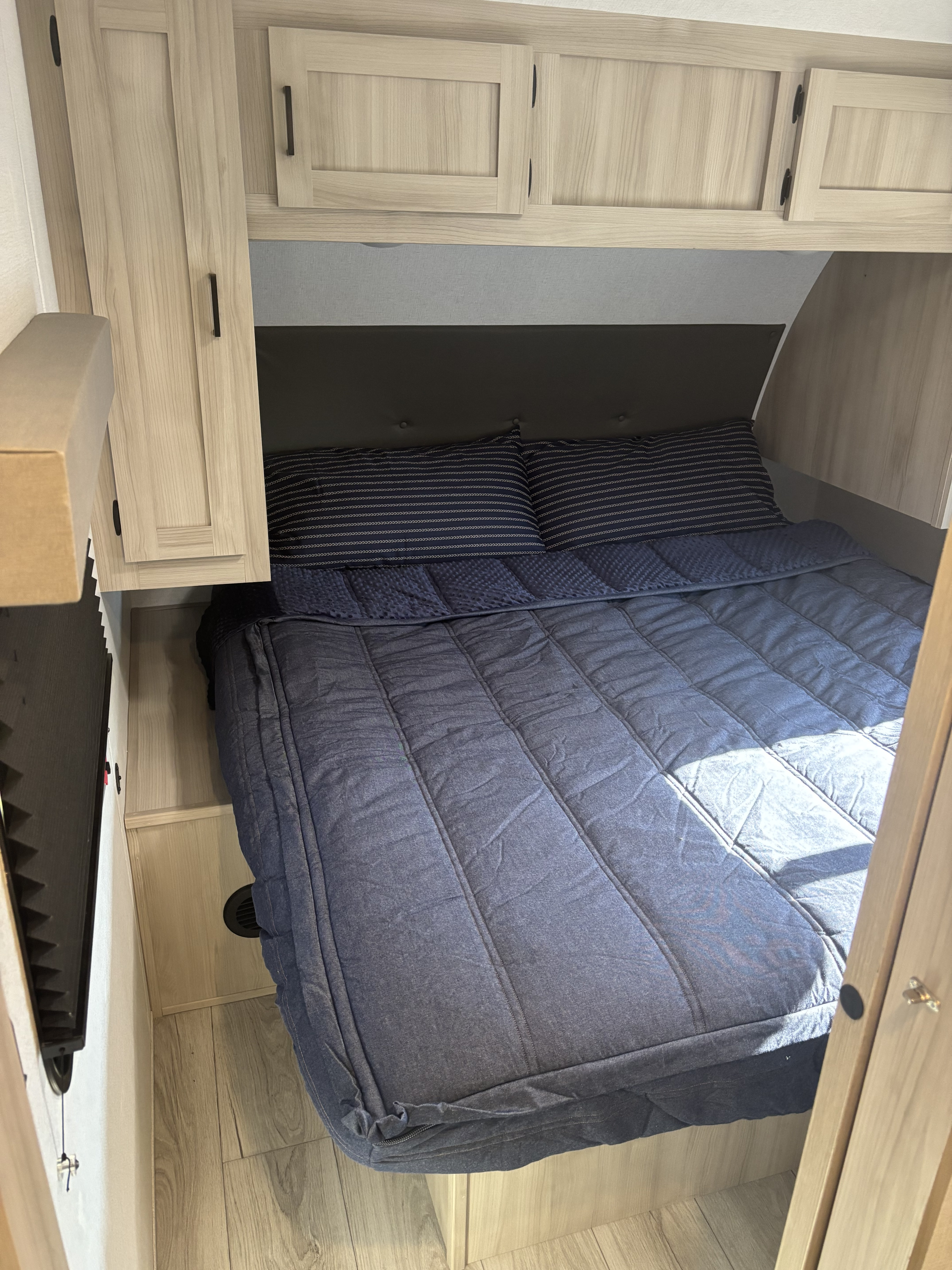 Cozy RV rental bedroom featuring a dark blue bed, striped pillows, and light wood cabinetry for compact travel comfort.. East to West Della Terra 291bh 2024