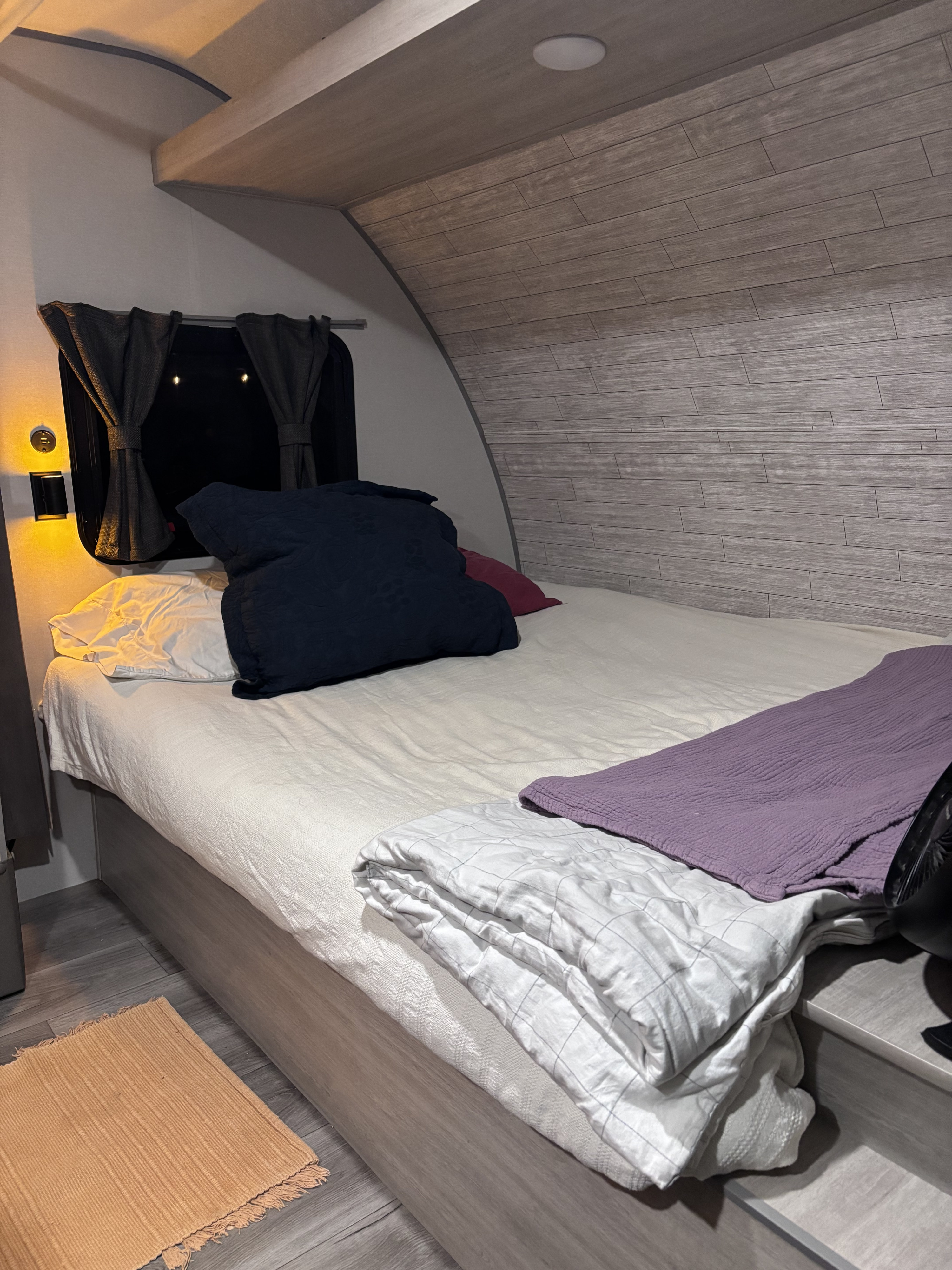 RV rental bedroom with a comfortable bed, dark blue & white pillows, blankets, and a side lamp by the window.. Coachmen 184BH 2025