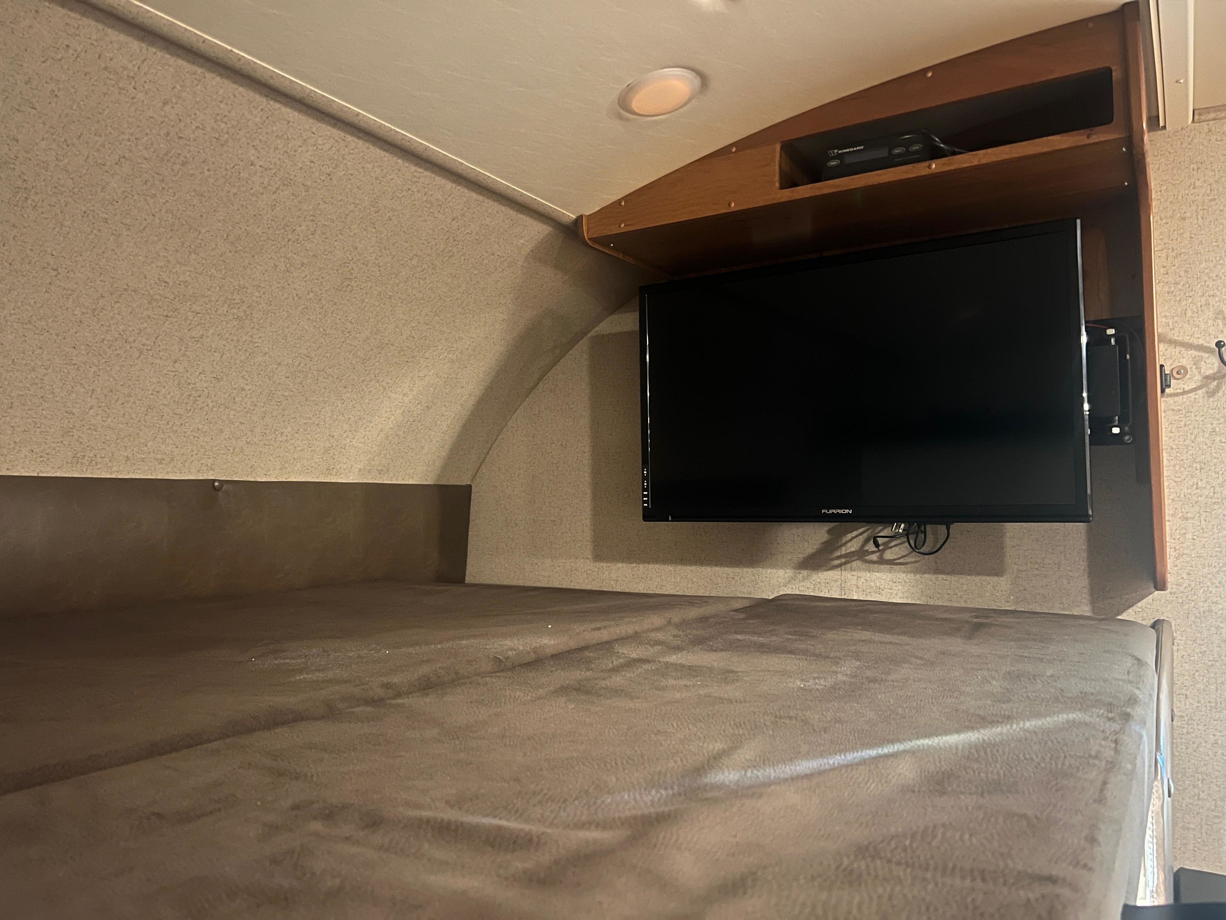 RV rental sleeping nook featuring a textured bunk bed, wall-mounted Furrion TV, and Winegard entertainment console.. Jayco Greyhawk 2016