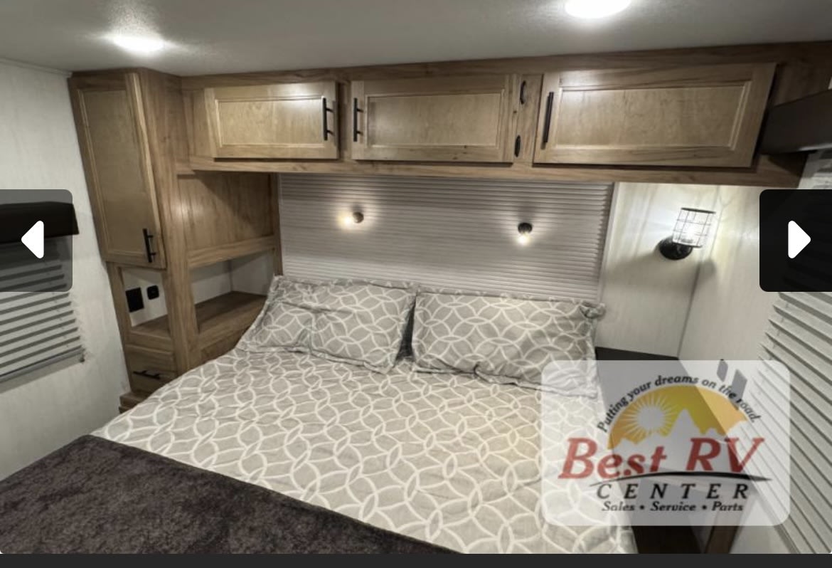 Cozy RV rental bedroom featuring a bed with geometric bedding, wooden overhead cabinets, and practical side storage with lighting.. Forestriver Timberwolf 20OG 2025