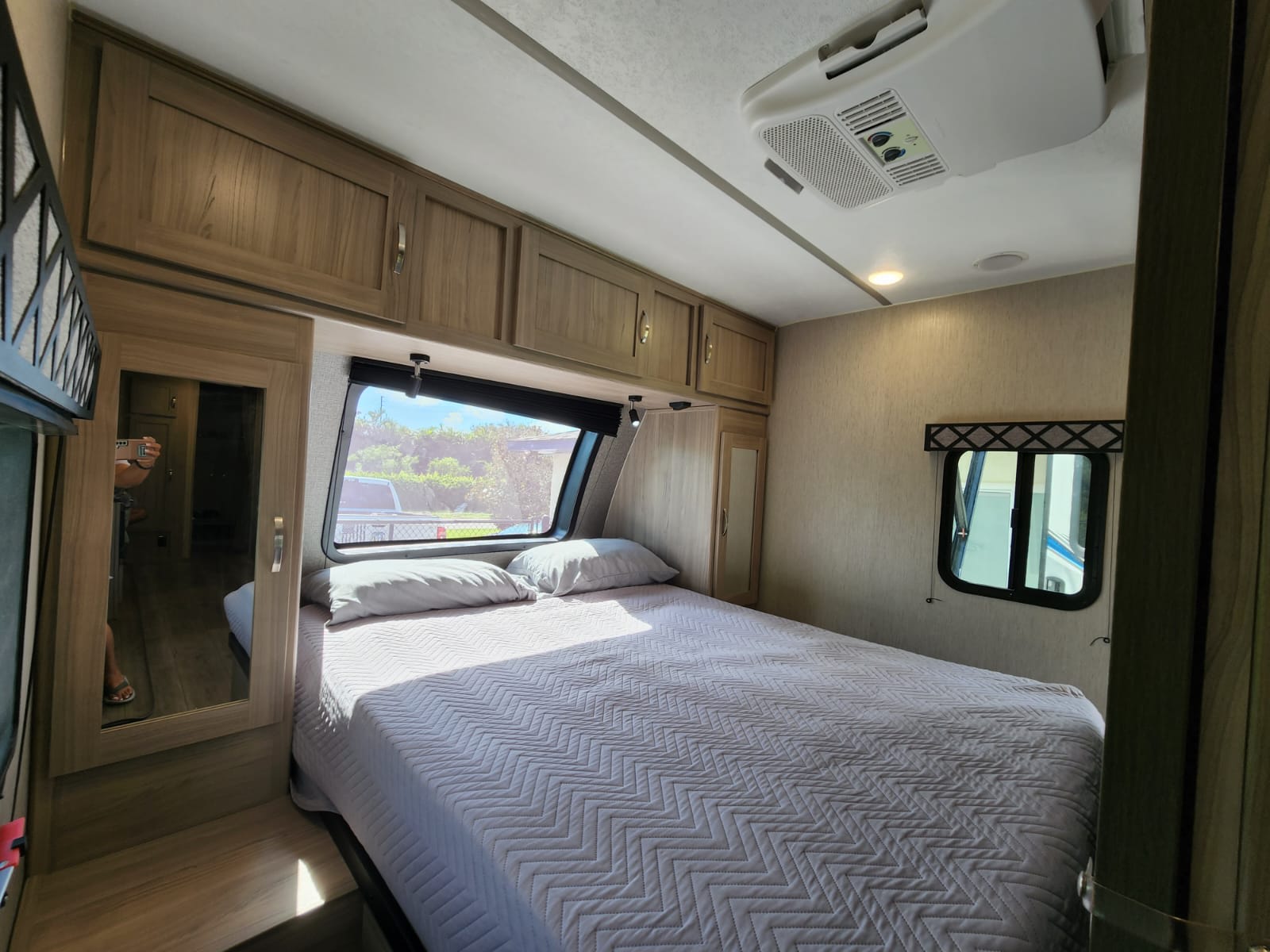 Bright and inviting RV rental bedroom featuring a large bed, overhead cabinets, front window view, and mirrored closet for comfort.. Coachmen 292BHDS 2021