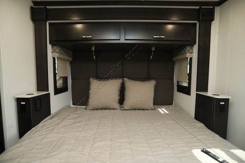 Cozy RV rental bedroom featuring a large bed, dark wood overhead cabinets, and built-in side tables with controls.. DX3 DX3 Motorhome 2022