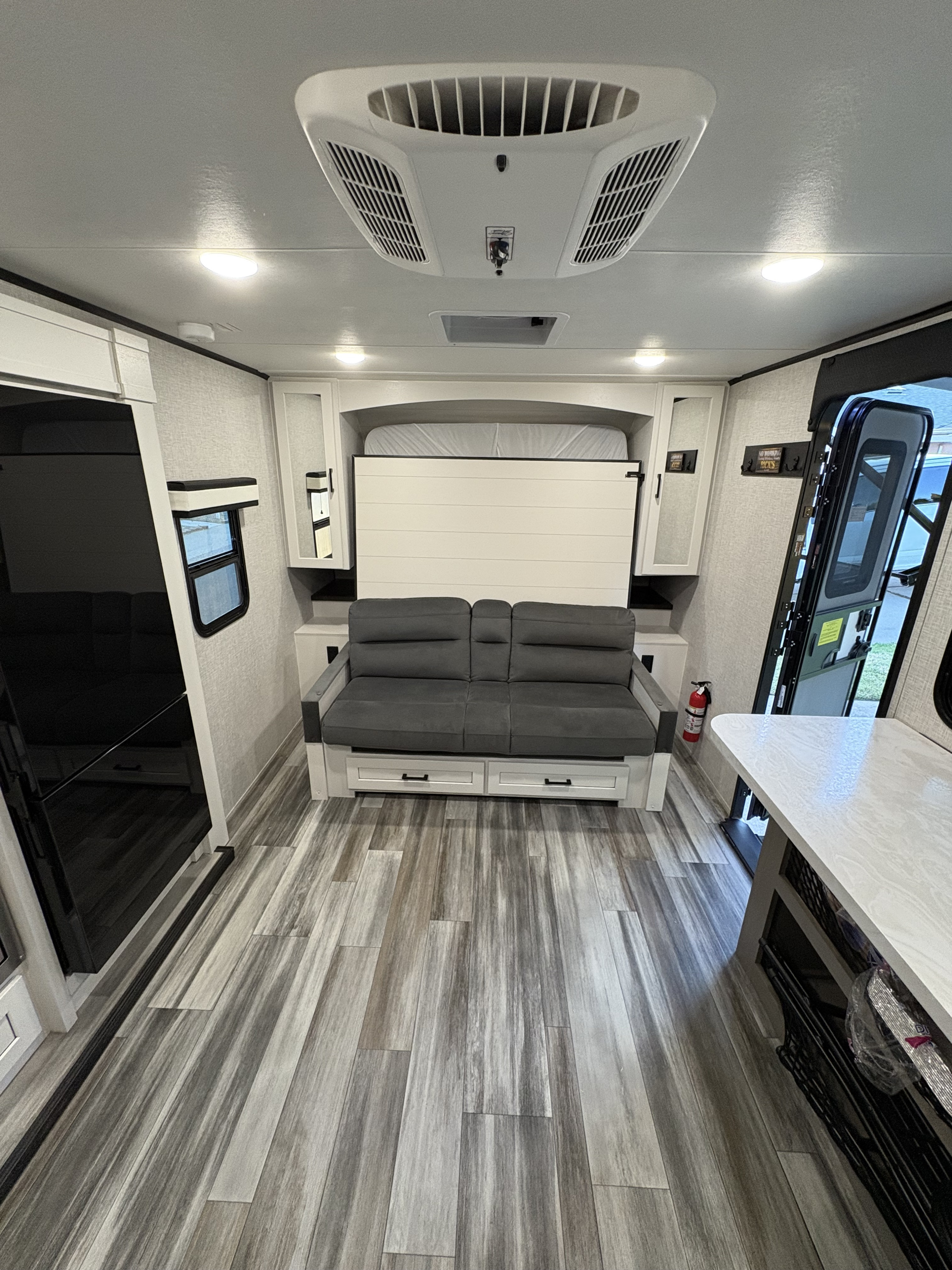 Inside this cozy RV rental: a flexible living space with a murphy bed, sofa, AC unit, and wood-grain flooring.. Jayco Jay Feather 18MBH 2025