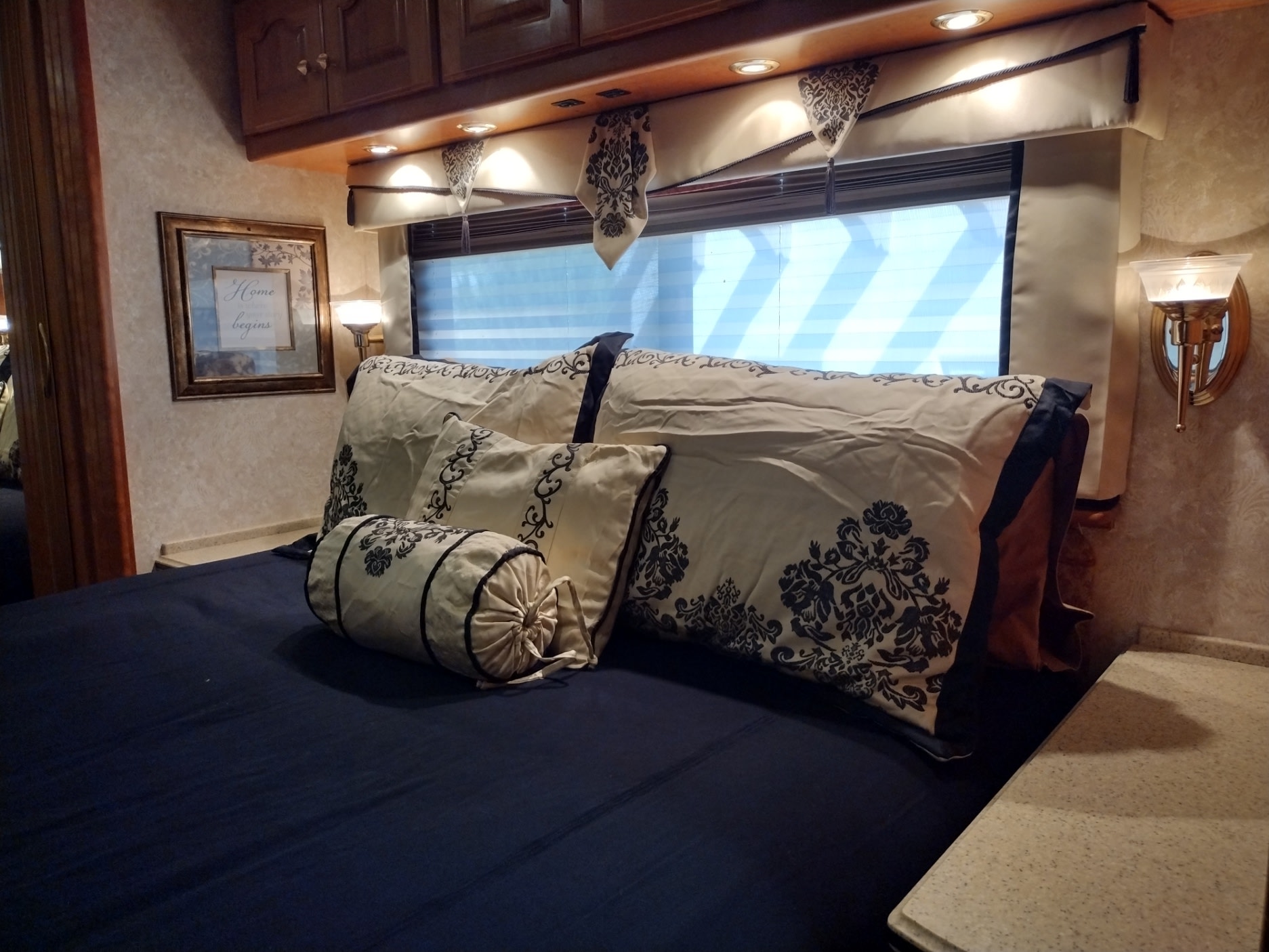 Inside an RV rental bedroom: bed with patterned pillows, overhead lights, a window, and wall art creating a cozy space.. Country Coach Allure 470 2005