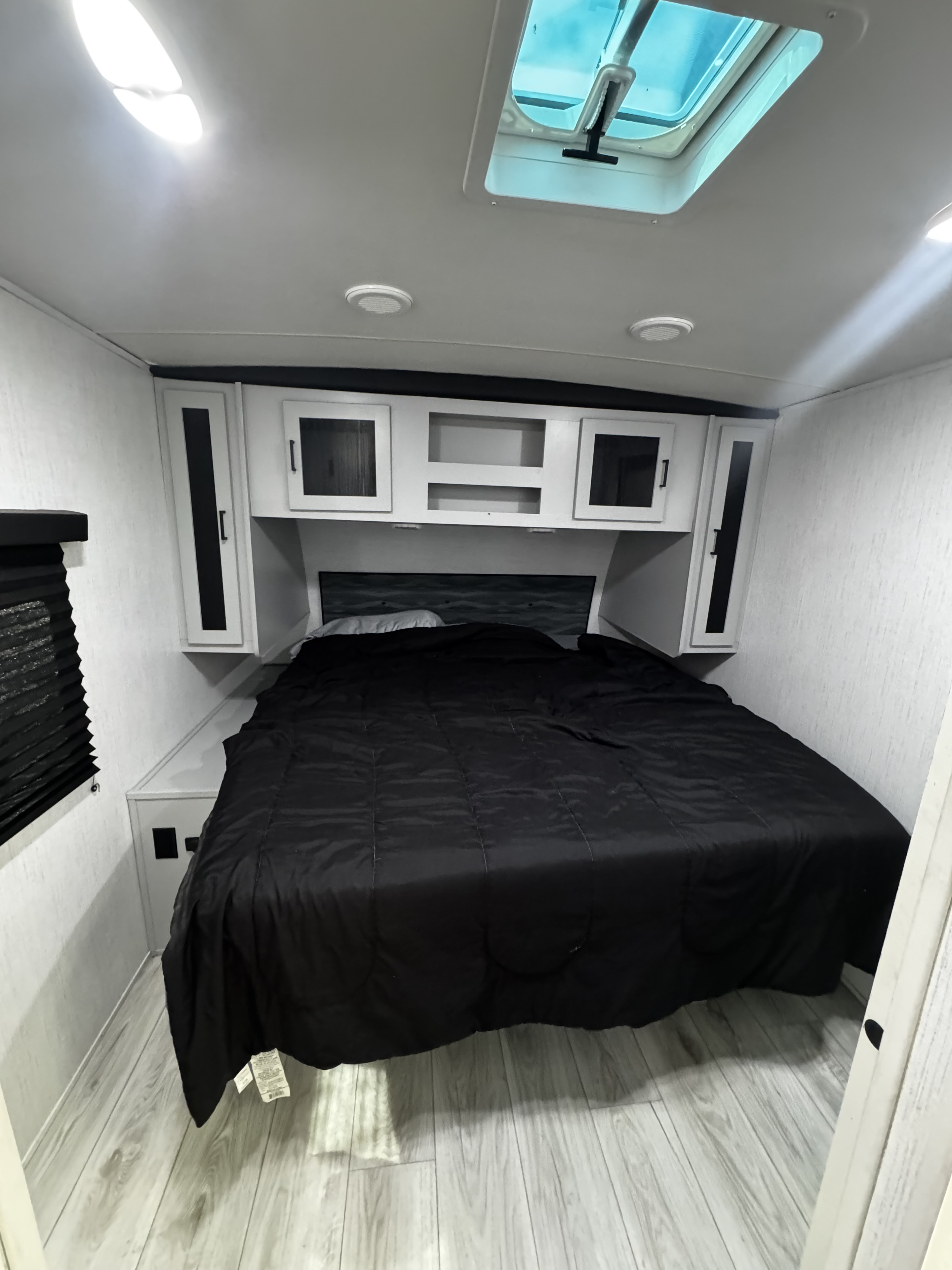 Spacious RV rental bedroom with a large black bed, white cabinets, skylight, and light wood-look flooring.. Heartland RVs North Trail 2022