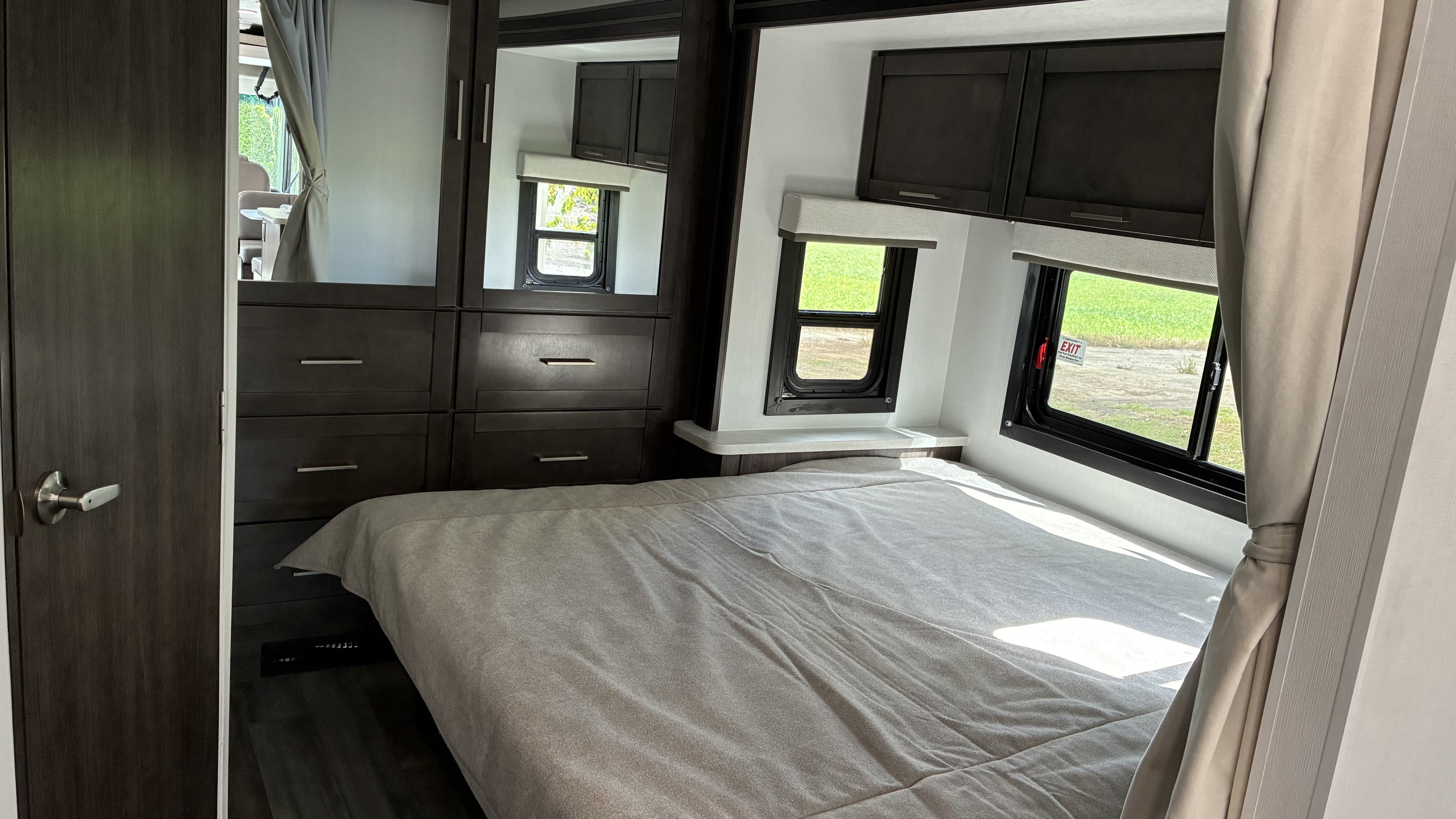 Cozy RV rental bedroom with a light bed, dark wood storage, and windows looking out to a green field.. Jayco Alante 27 ASE 2026