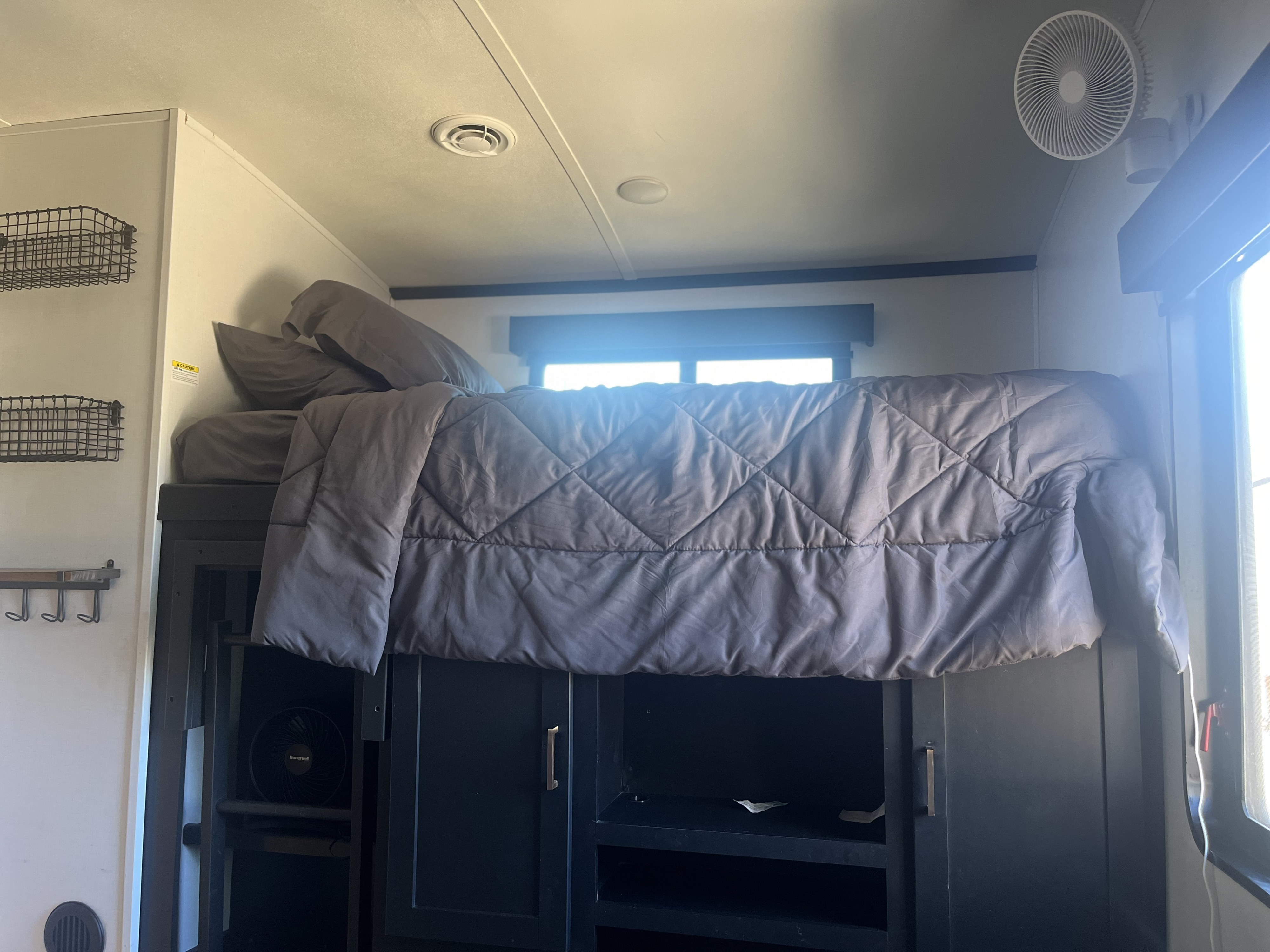RV rental interior: A compact bunk bed with gray bedding, built-in storage cabinets, and a fan, optimizing small living space.. Keystone RV Outback 2022