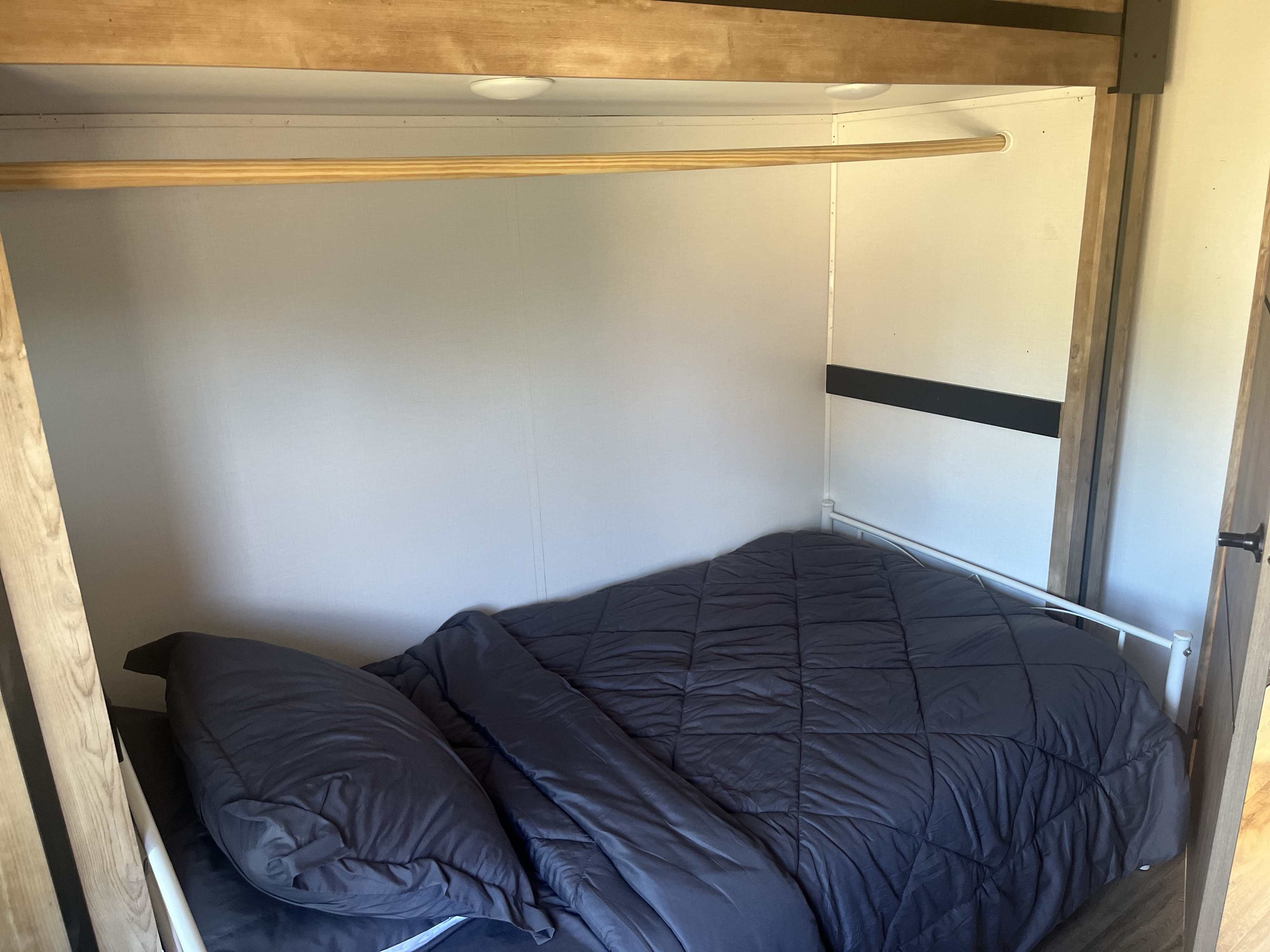 Compact RV rental bunk bed with a dark comforter, pillow, and an overhead clothes rod.. Keystone RV Outback 2022
