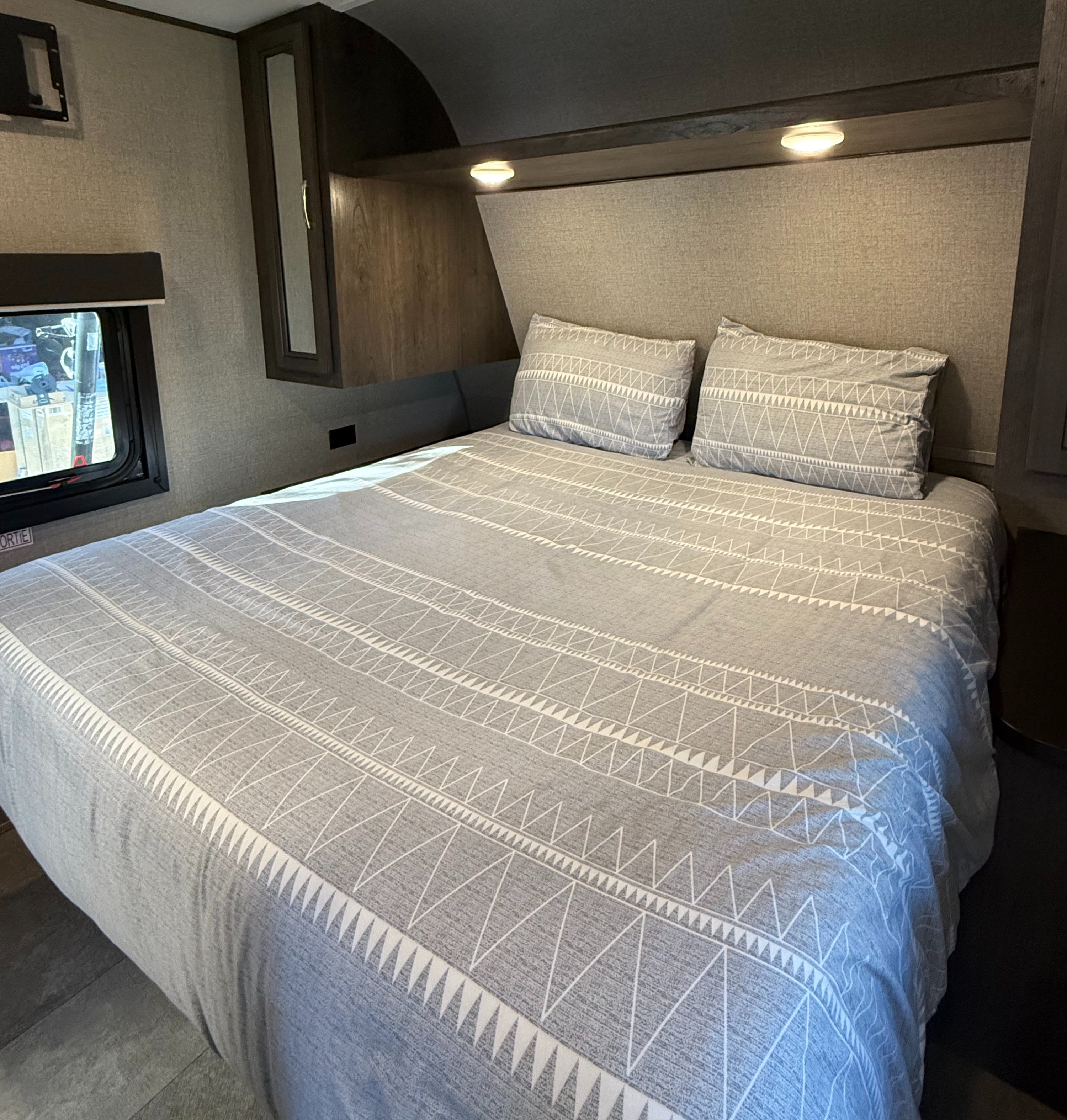 Cozy RV rental bedroom featuring a comfortable bed with a light grey geometric patterned comforter, pillows, and ambient lighting.. Jayco Jay Flight SLX Rocky Mountain Edition 2020