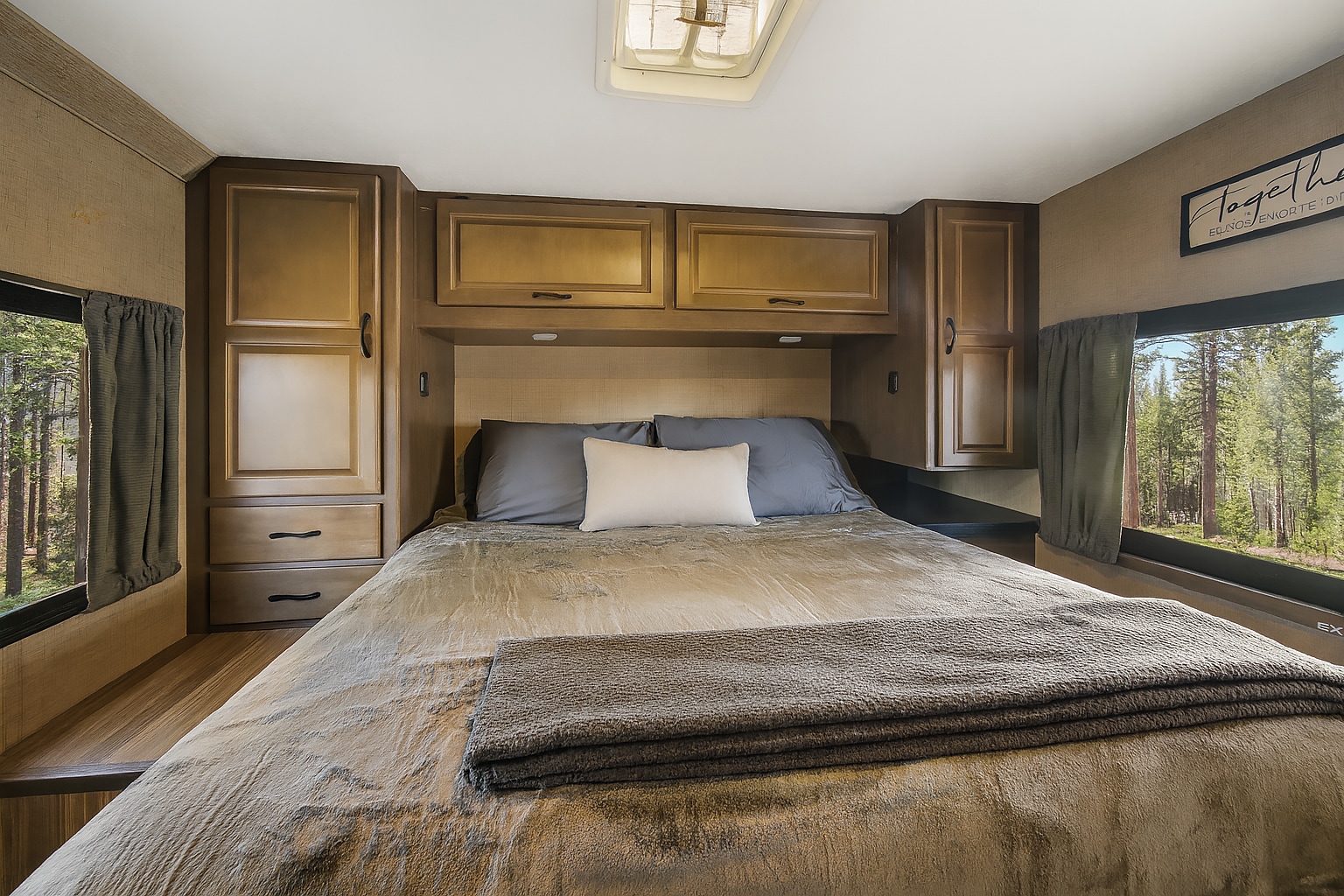 Comfortable RV rental bedroom featuring a cozy bed, overhead storage, and scenic forest views from both windows.. Thor Majestic 2018