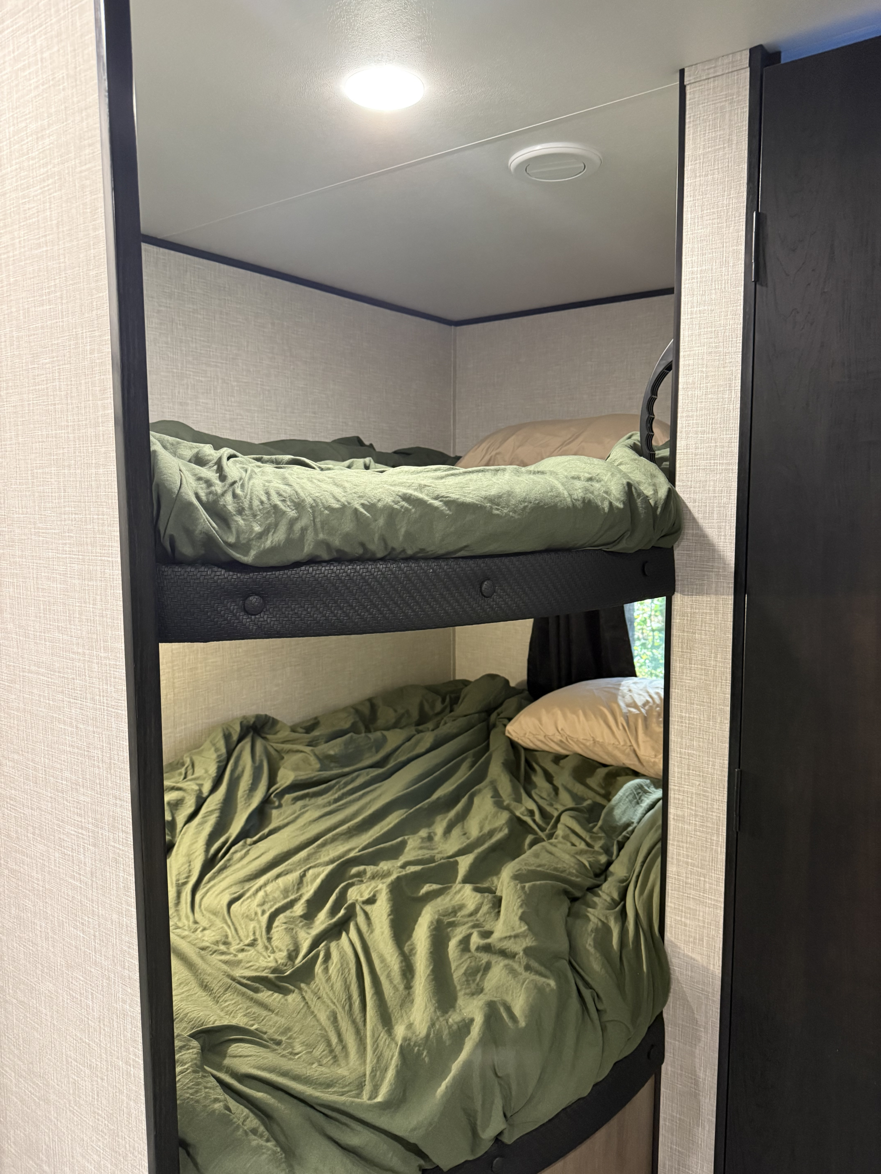 Inside a cozy RV rental: two bunk beds with olive green sheets & pillows, ceiling light, and vent.. Jayco Jay Flight SLX 2024