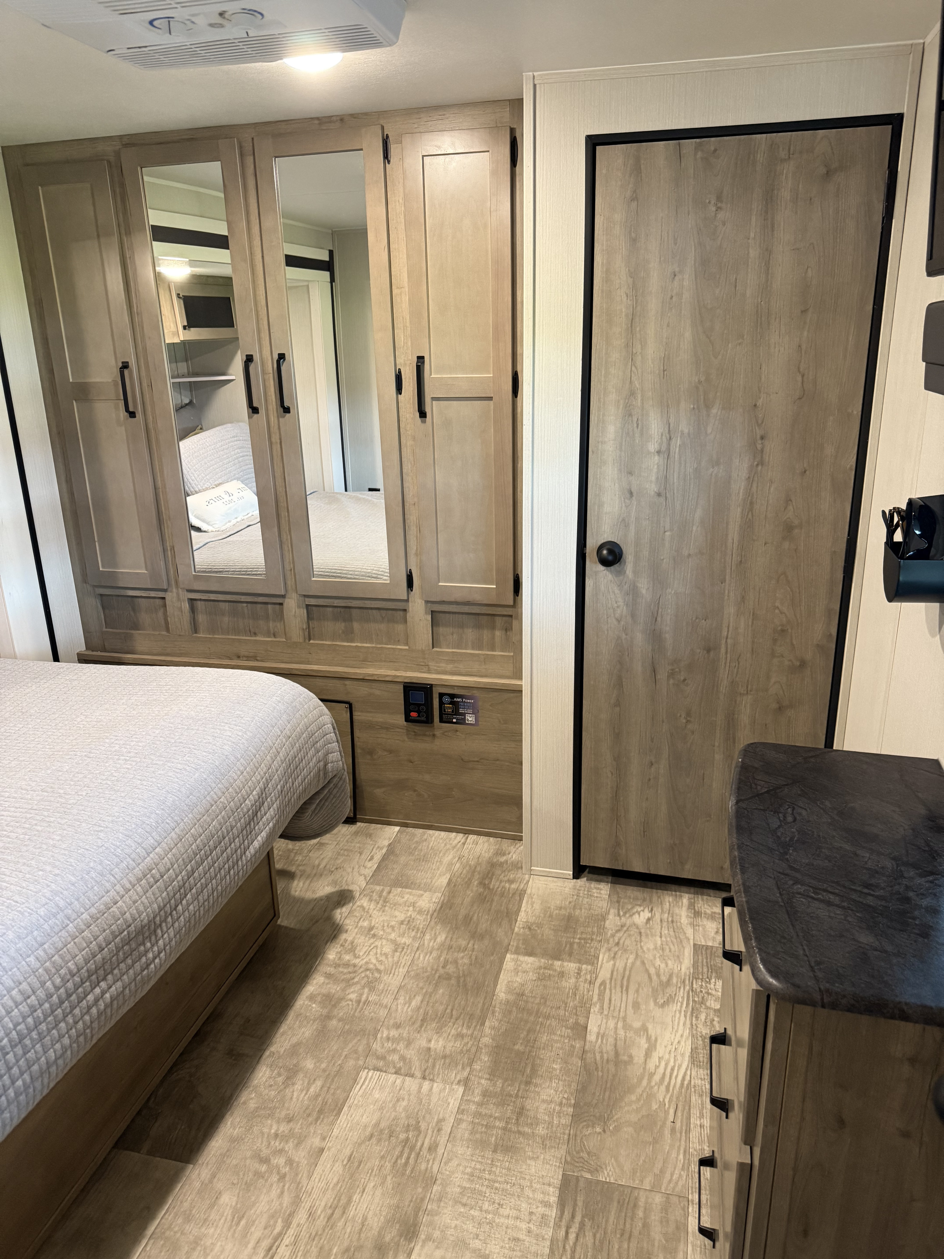 View of a modern RV rental bedroom, featuring a bed, large mirrored wardrobe, and light wood-look floor.. Forest River Palomino Puma 2024