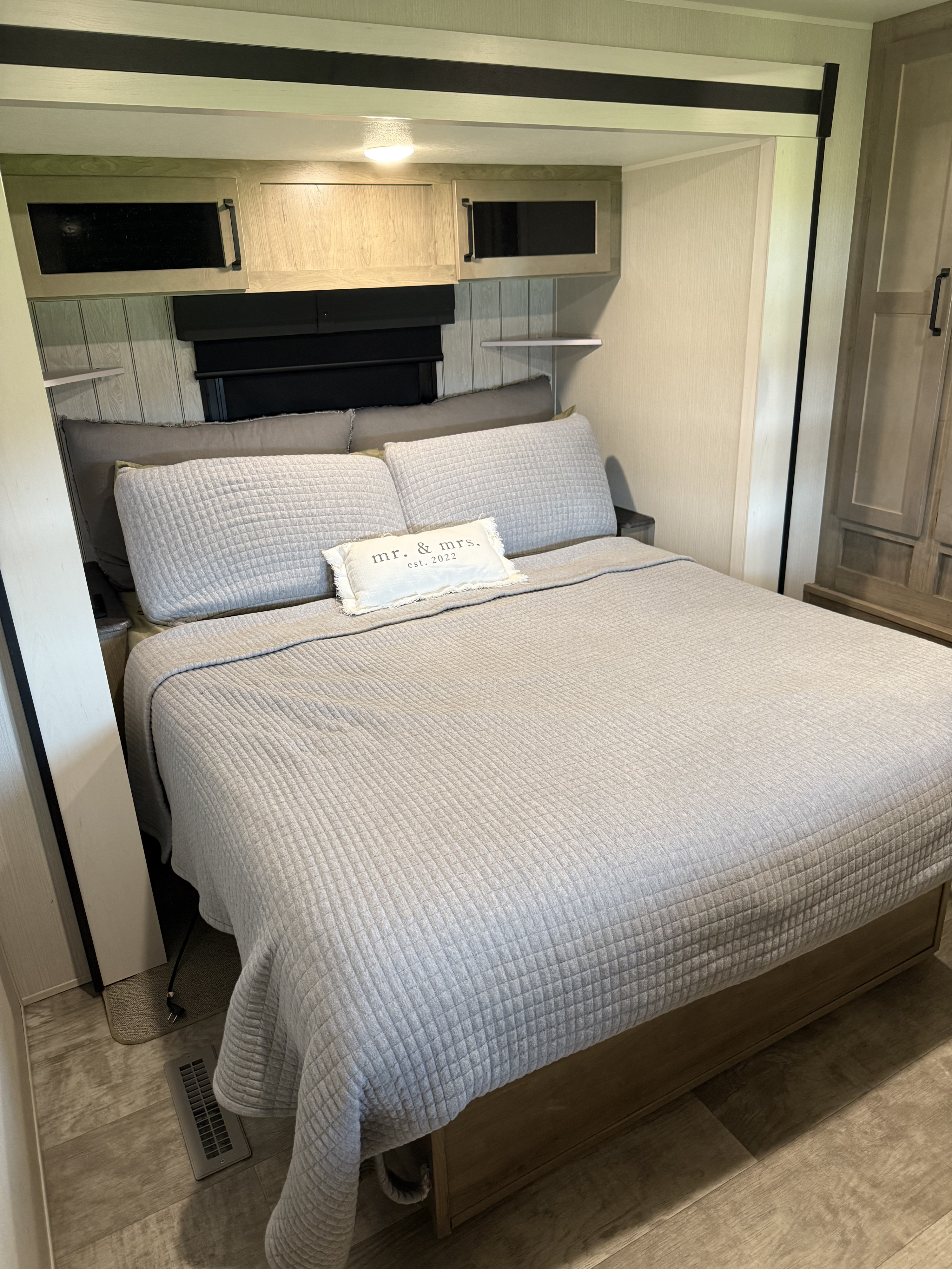 Cozy rv rental bedroom showing a bed with modern gray bedding, an accent pillow, overhead cabinets, and wood-look flooring.. Forest River Palomino Puma 2024