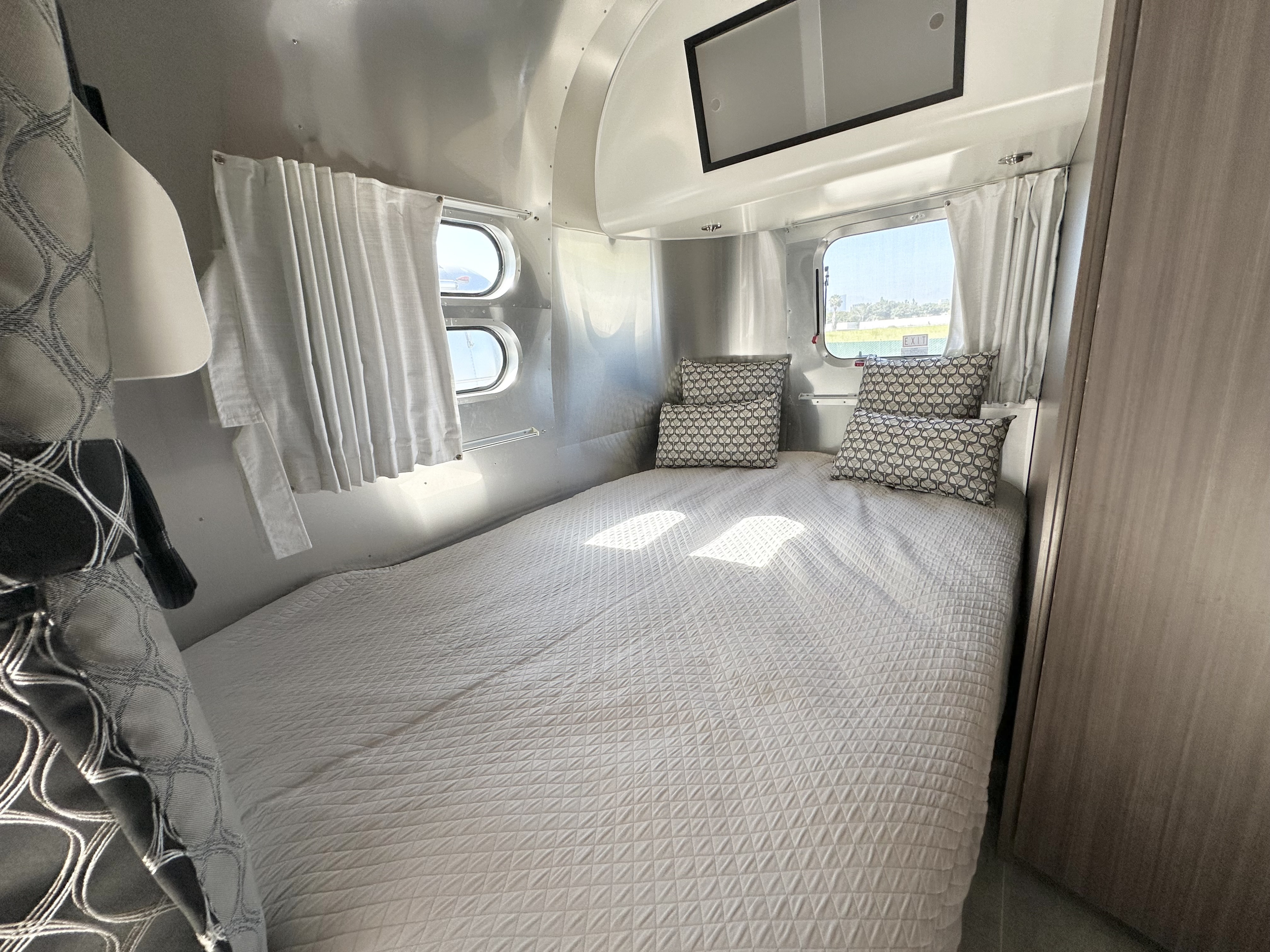 Bright RV rental bedroom featuring a quilted bed, patterned pillows, sleek metallic walls, and sunny windows for comfortable travel.. Airstream Caravel 2020