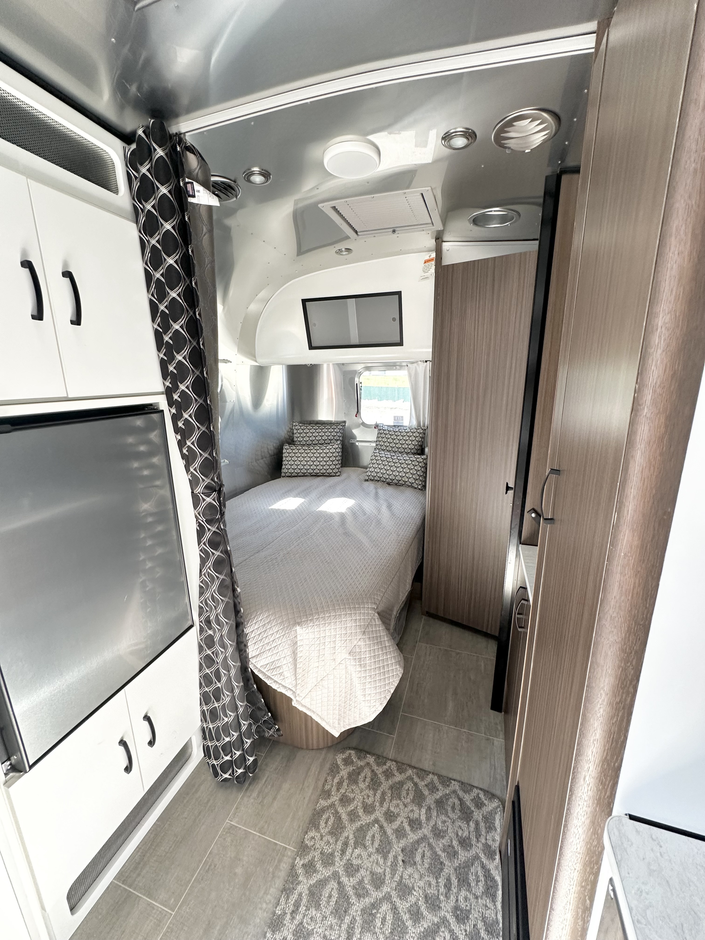 Modern RV rental bedroom with a quilted bed, geometric curtain, white cabinets, and wood accents, ready for adventure.. Airstream Caravel 2020