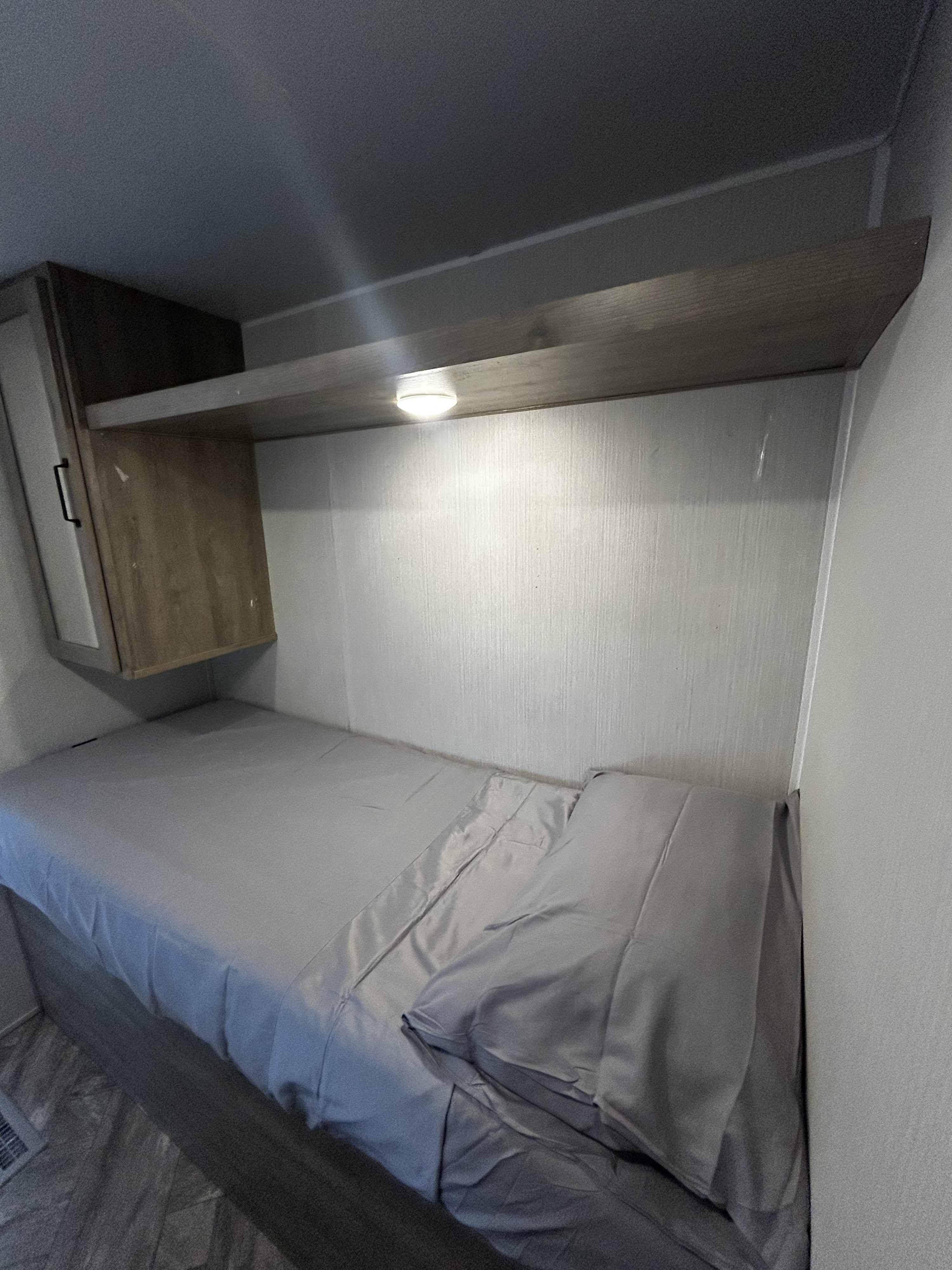 RV rental bunk bed with grey sheets, overhead shelf, and cabinet. Small, cozy sleeping area.. Palomino Puma 2023