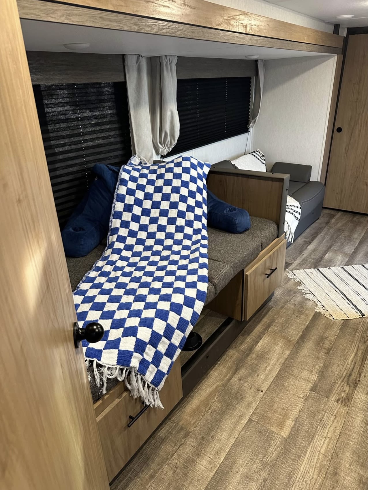 Inside an rv rental: a cozy bunk area with a blue/white checkered blanket, storage, seating, and wood floors.. Forest River Campsite reserve 25MW 2024